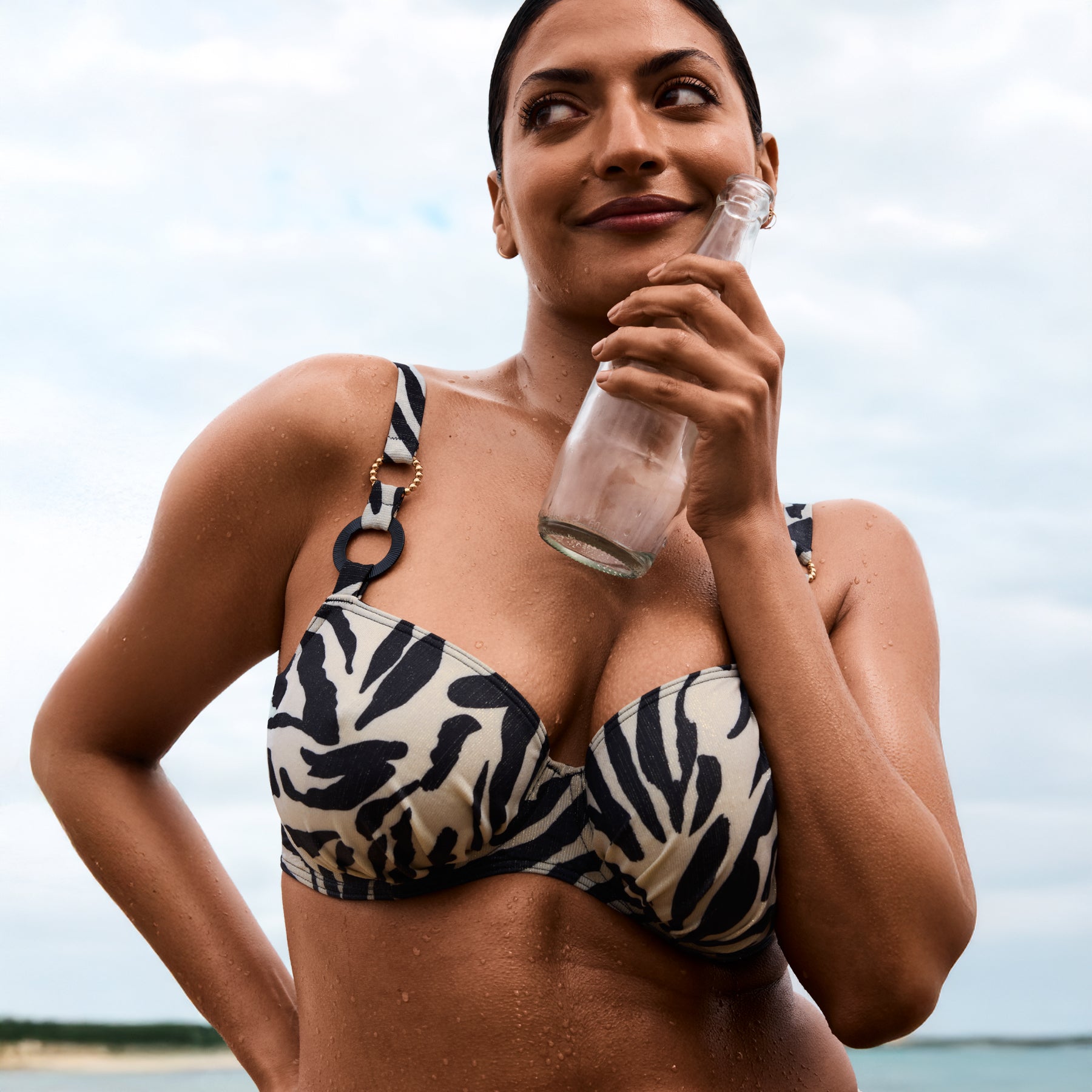 Woman wearing zebra print bikini top holding a glass bottle at the beach