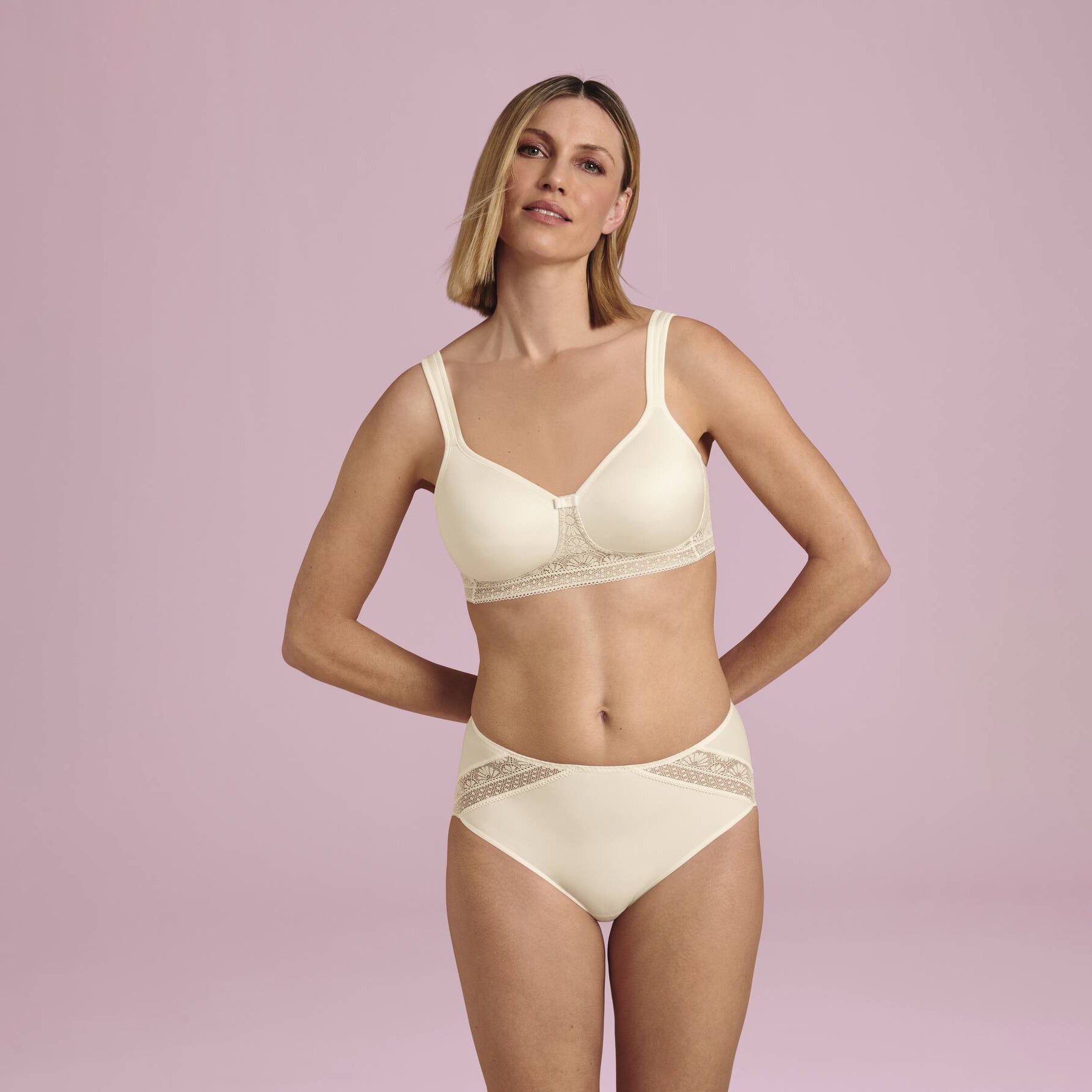 Woman wearing ivory seamless bra and matching brief with lace band detail, full body front view