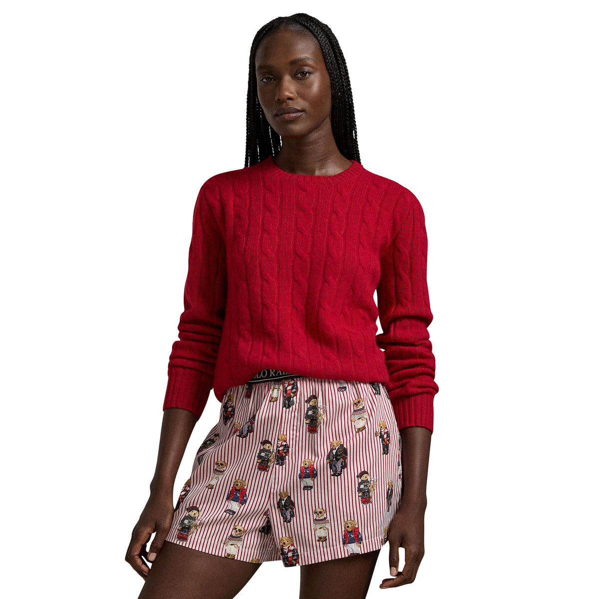 Model wearing Polo Ralph Lauren boxer sleep shorts with playful Polo Bear prints, red and white stripes, and a black branded waistband, paired with a red cable-knit sweater.