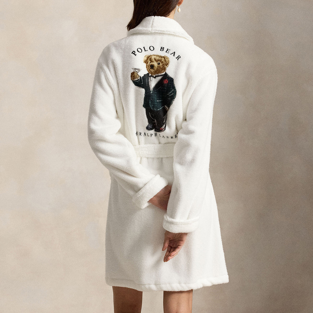 Rear view of Polo Ralph Lauren white fleece robe featuring a large embroidered Polo Bear dressed in a tuxedo, shawl collar, long sleeves, and adjustable waist belt.
