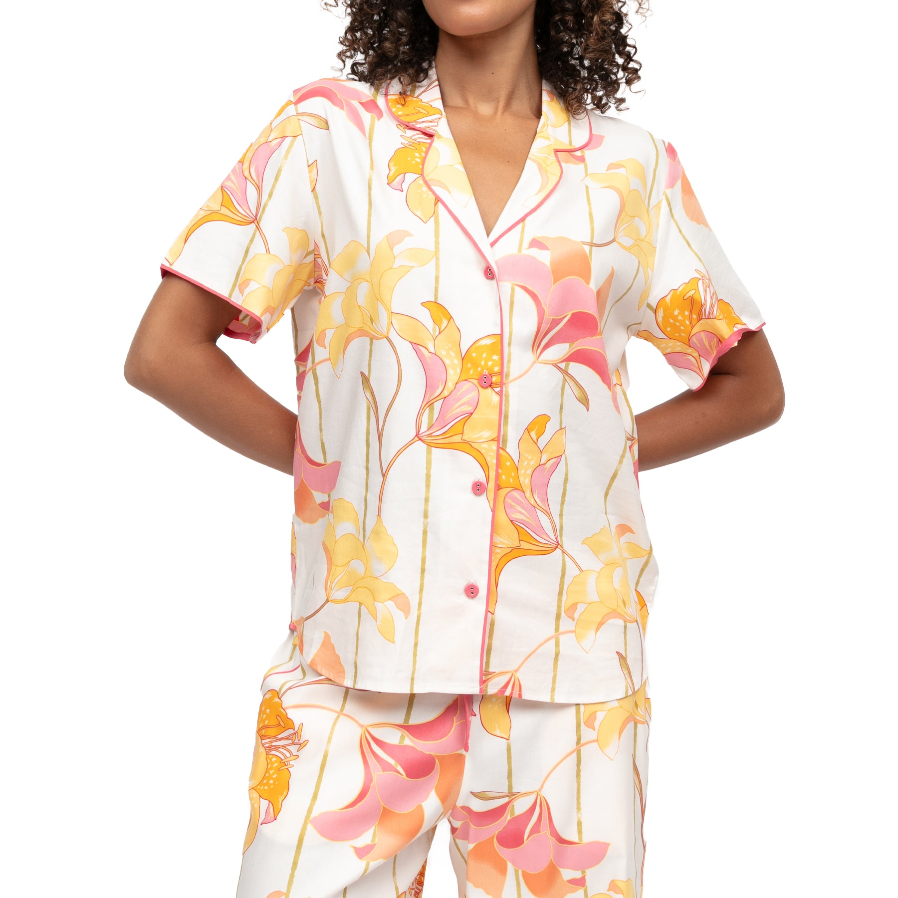 Close-up of short sleeve floral pyjama top with pink piping and button front in yellow and coral lily print on white background
