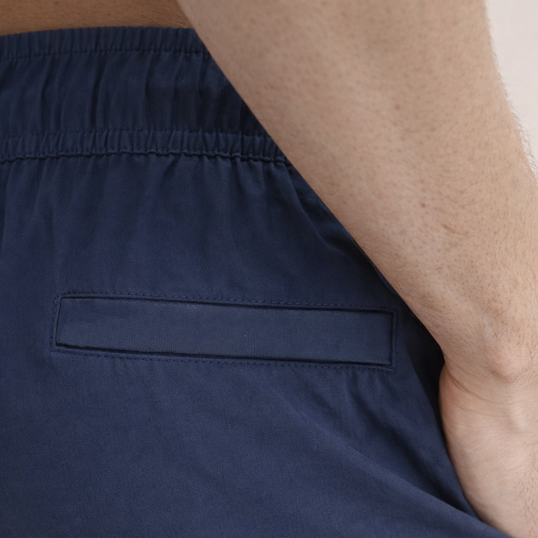 Close-up of navy swim shorts back welt pocket detail with elastic waistband.