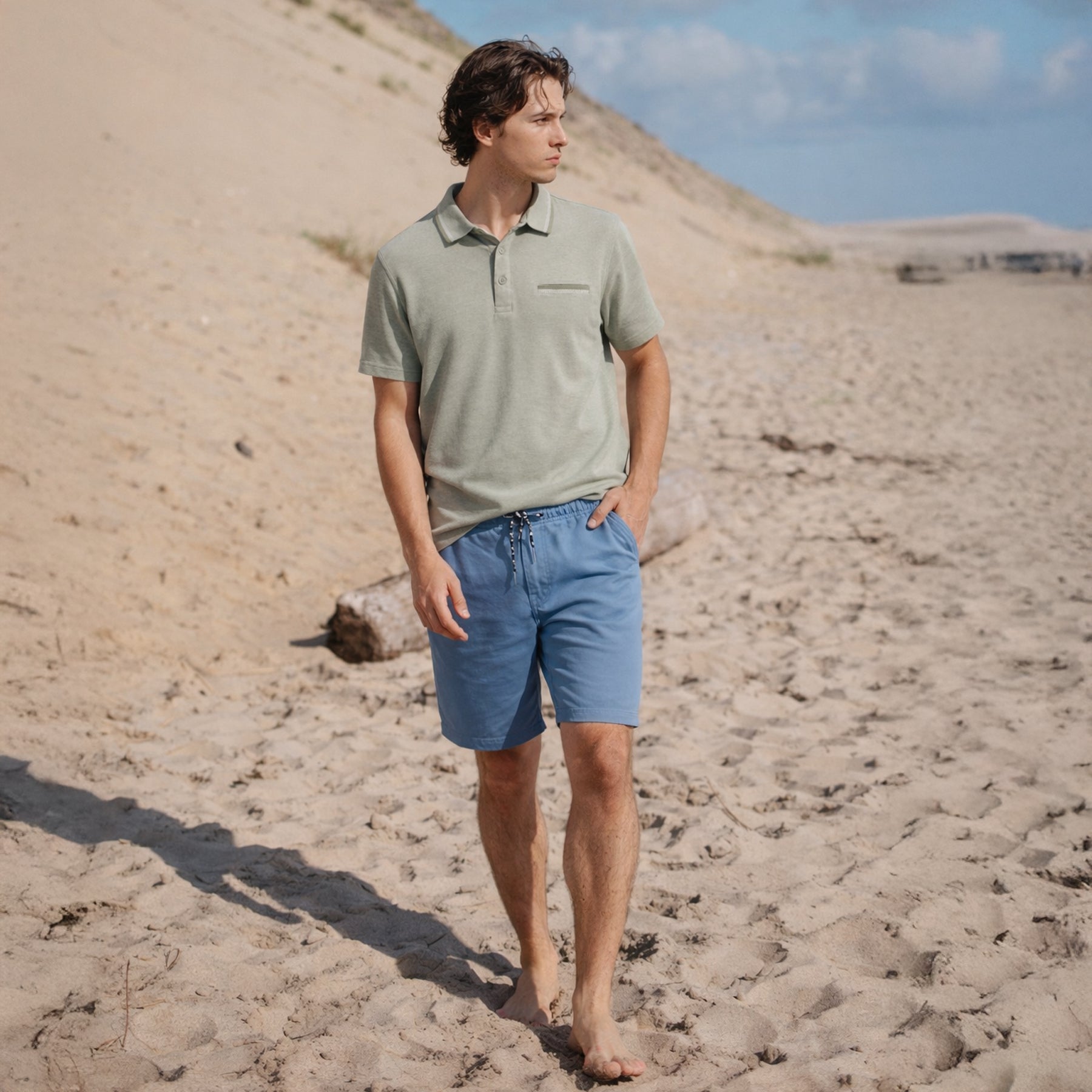 Men wearing sage green polo shirt and blue shorts walking barefoot on sandy beach