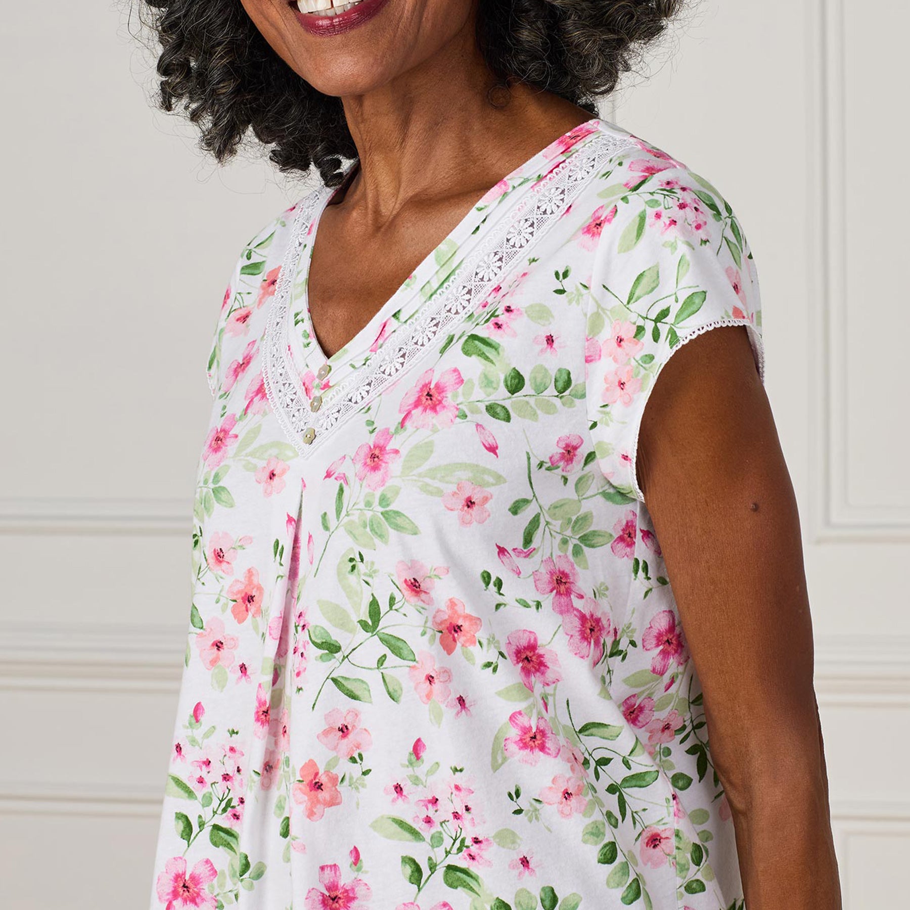 Close-up of a woman wearing a white cotton nightgown with a pink and green floral print and lace-trimmed V-neck.
