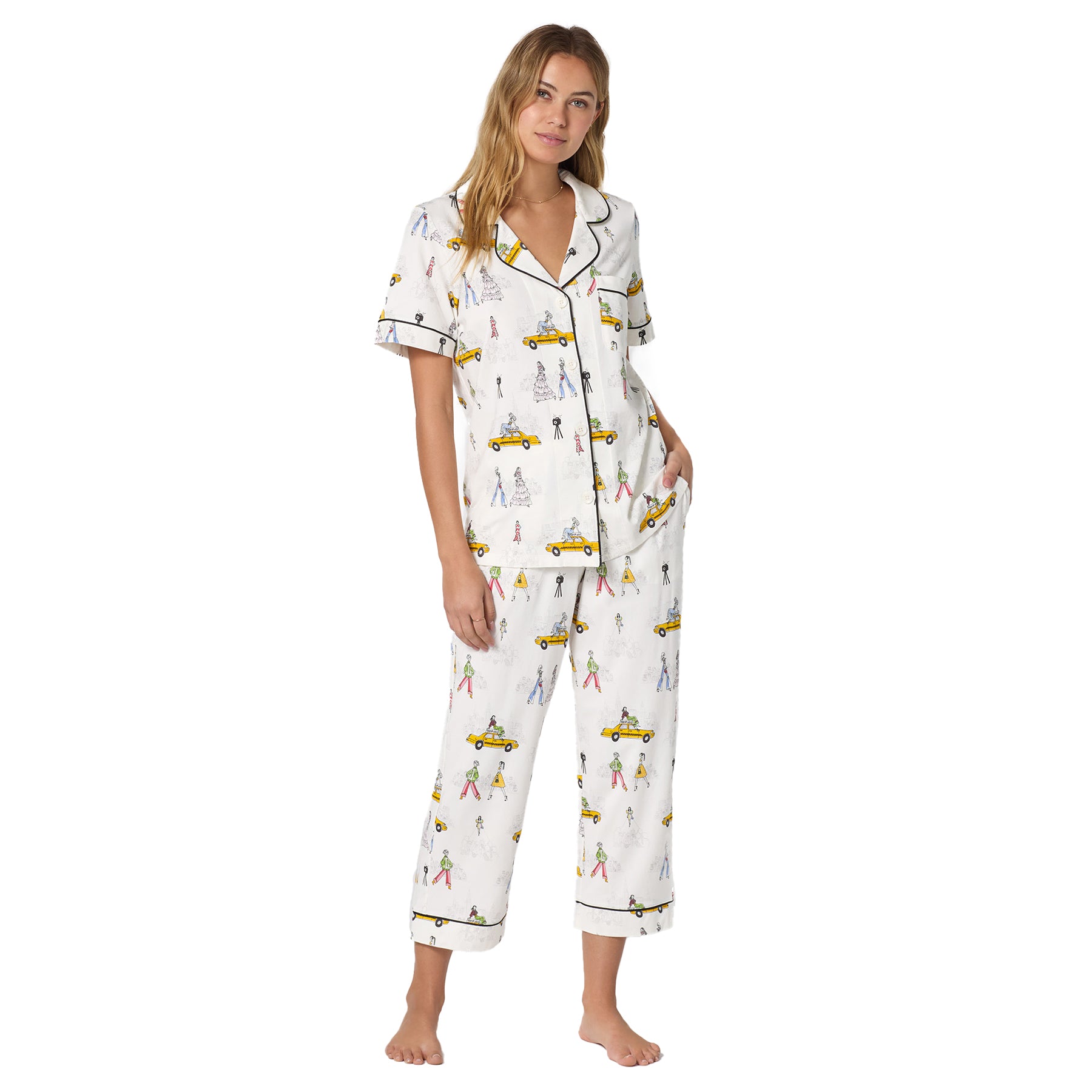 Front view of a model wearing a short sleeve button-up pyjama set with cropped pants in a fashion week print on a white background.