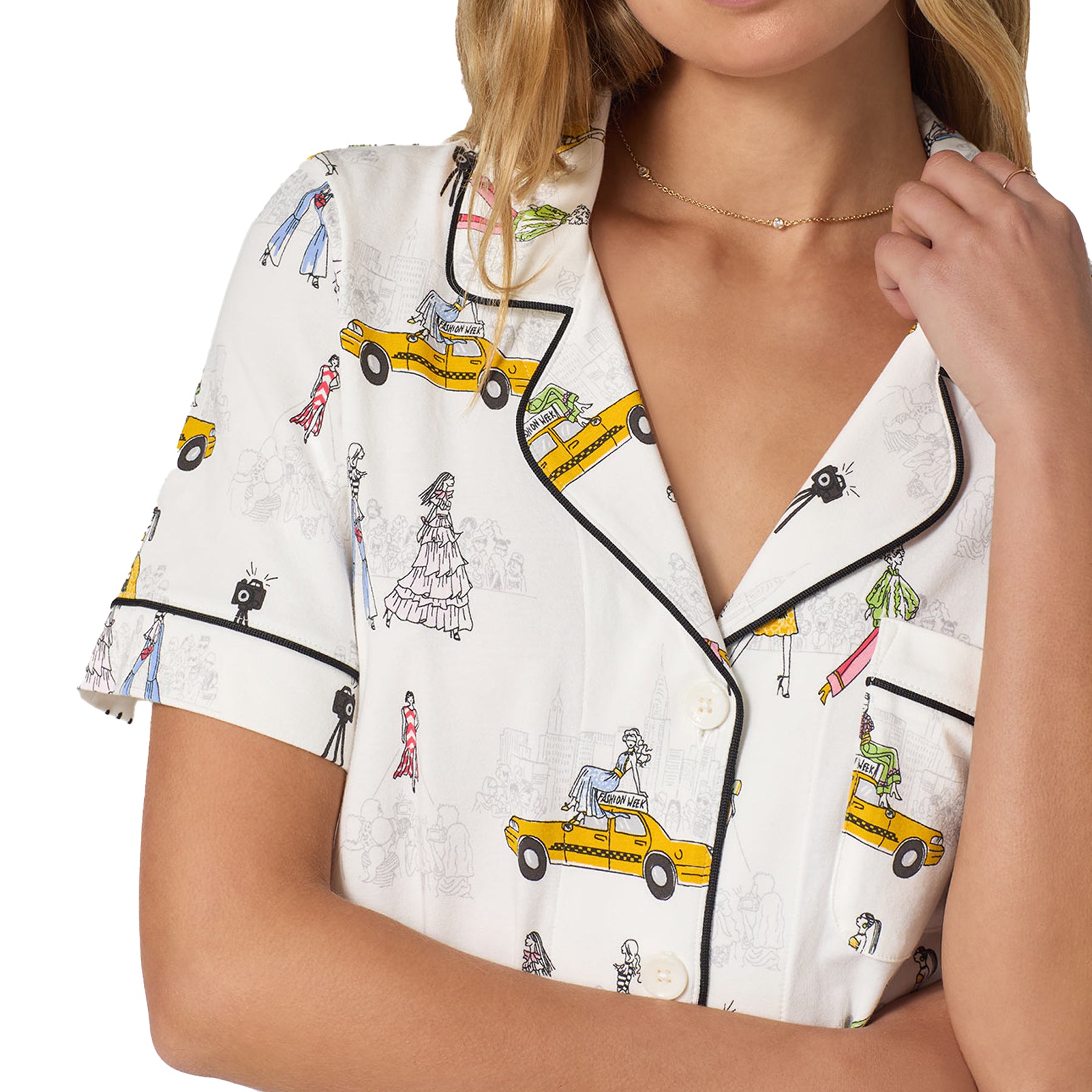 Close-up of the pyjama top showing the collar, buttons, black piping trim, and detailed fashion week illustration print with yellow taxis and stylised figures.