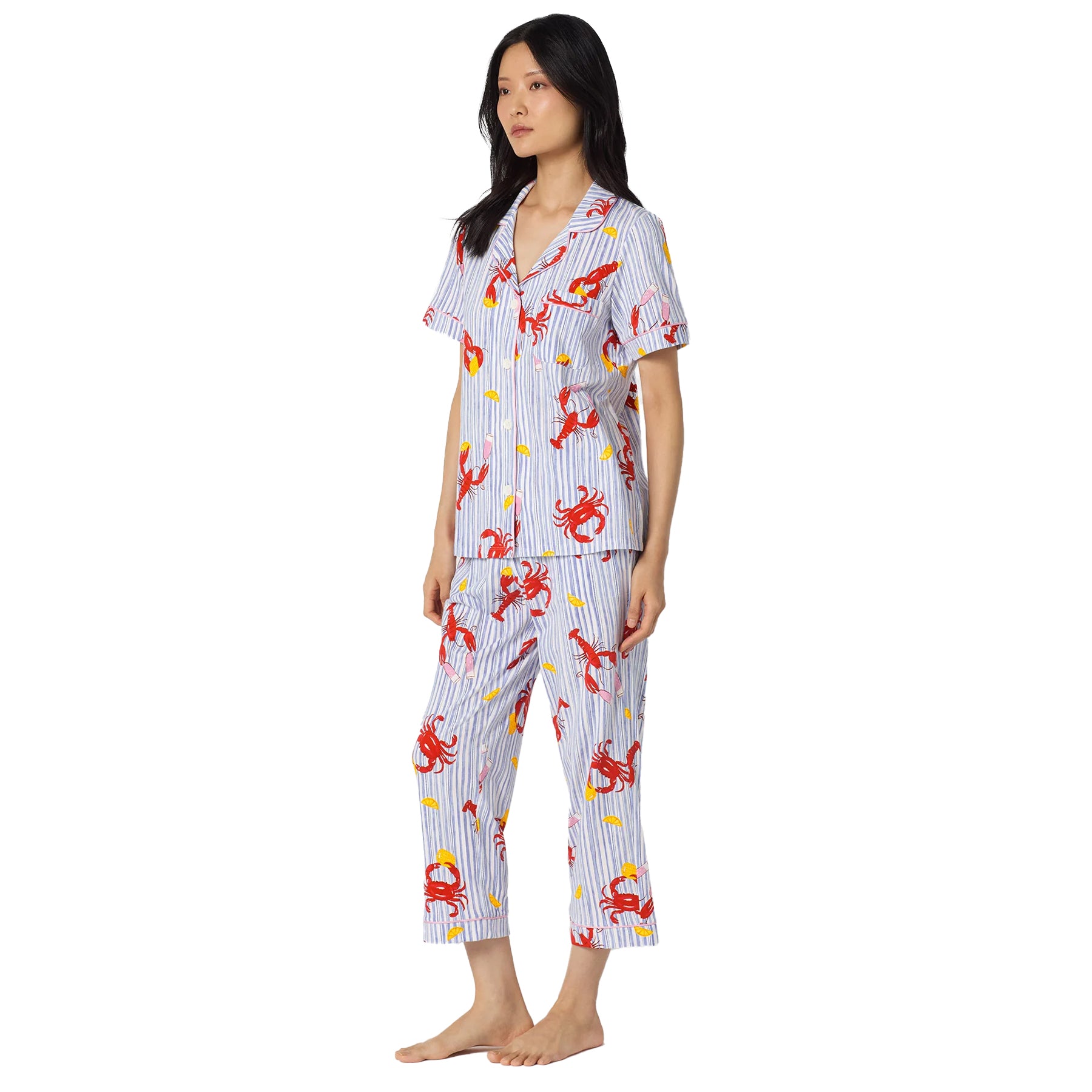 Woman wearing a lightweight blue striped sleepwear set with lobster and crab print, pink piping accents, and cropped pants.