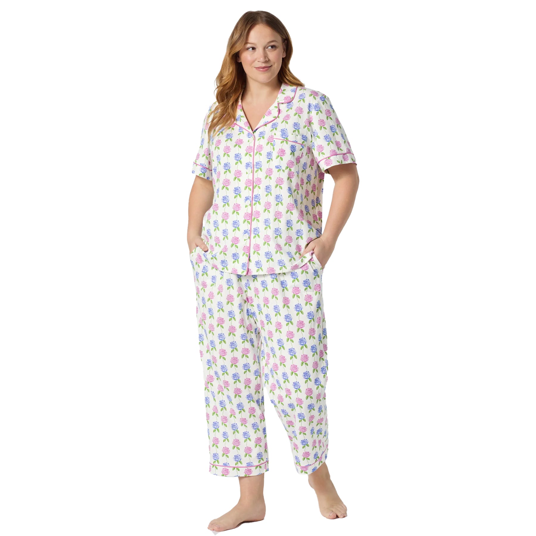 Woman wearing a classic white hydrangea print pyjama set with pink piping detail, short sleeves, and cropped straight-leg pants.