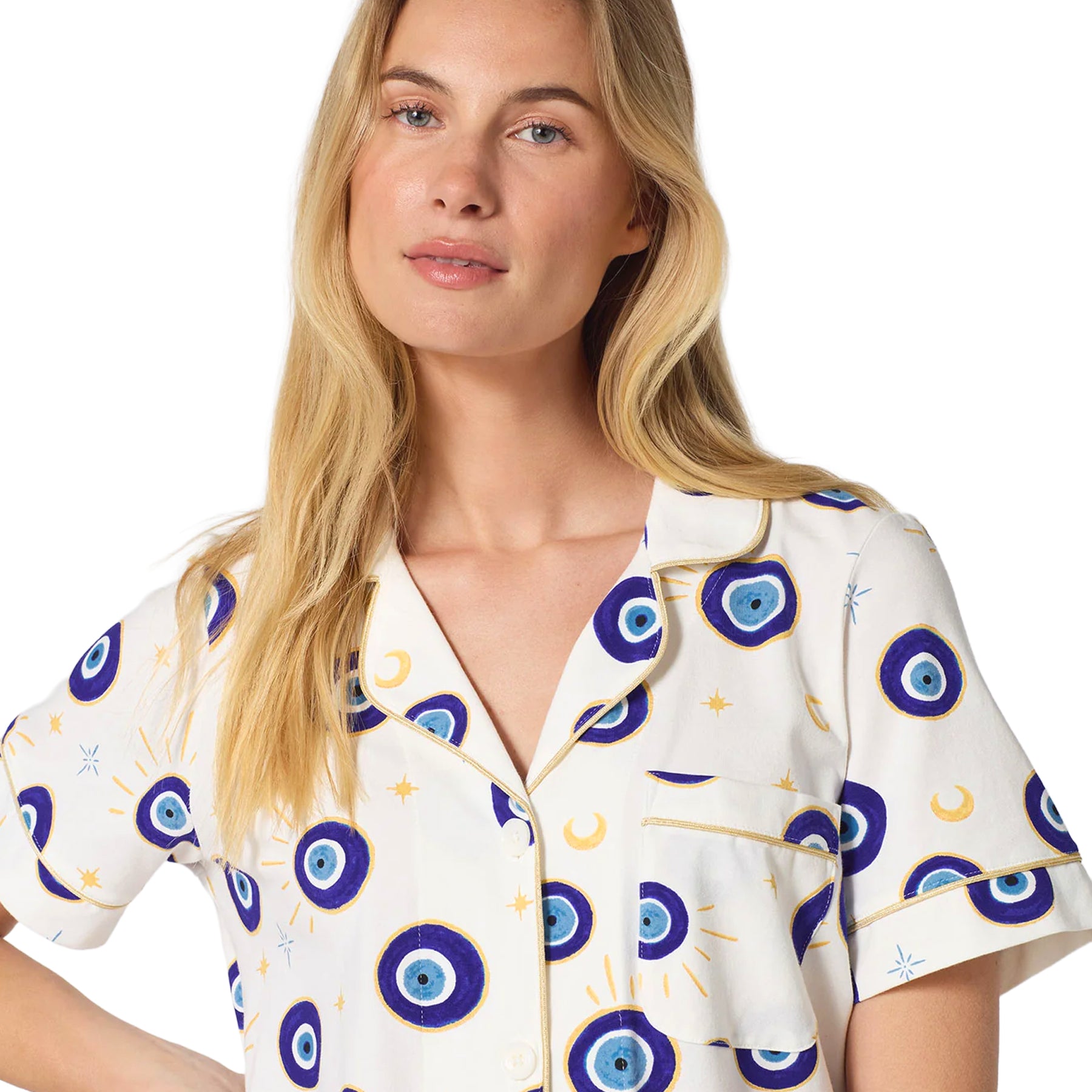 Close-up of an ivory pajama top featuring blue evil eye and celestial motifs, a notched collar, chest pocket and gold piping.