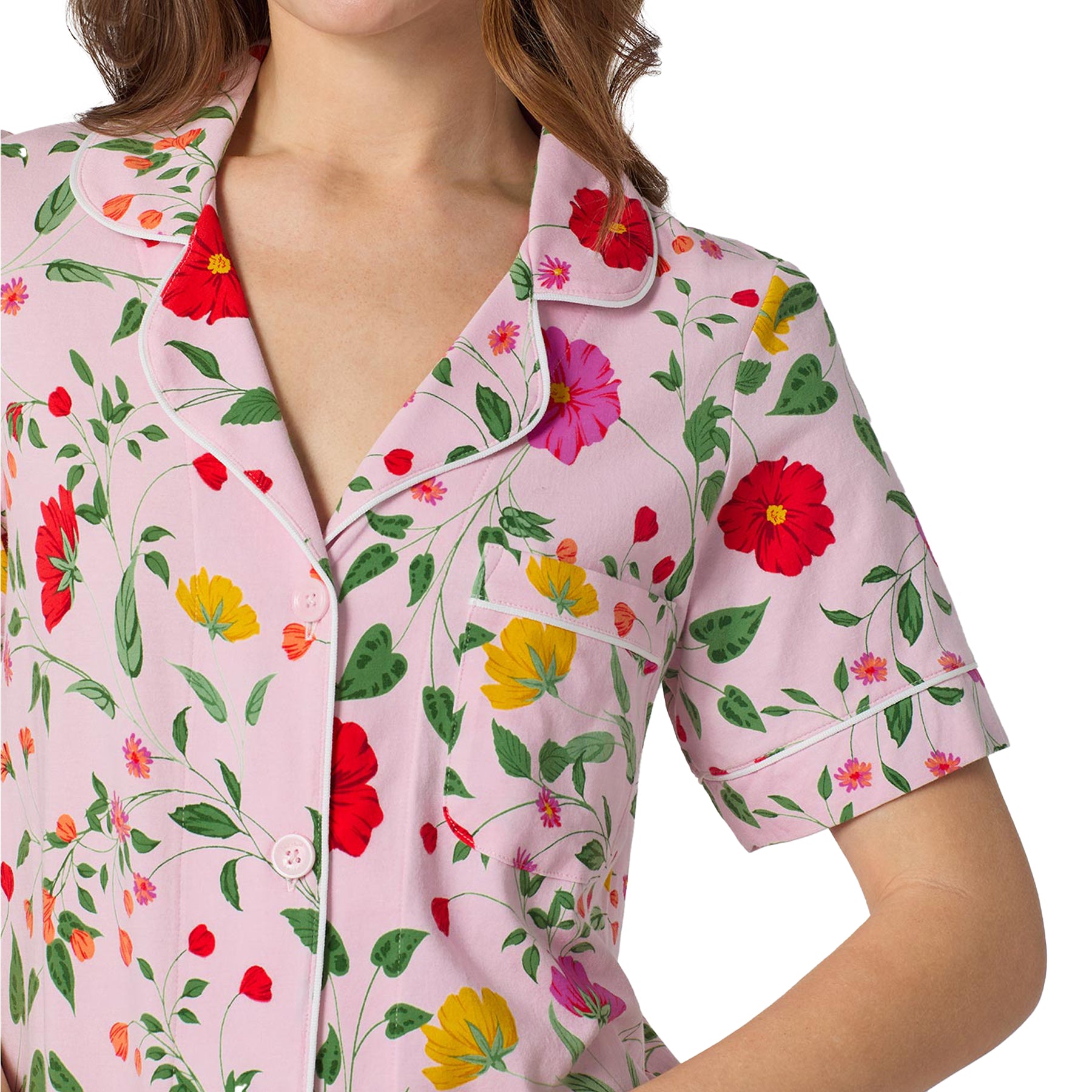 Close-up of pink floral short sleeve pajama top with contrast piping and button-front detail in vibrant red, yellow and green botanical print.
