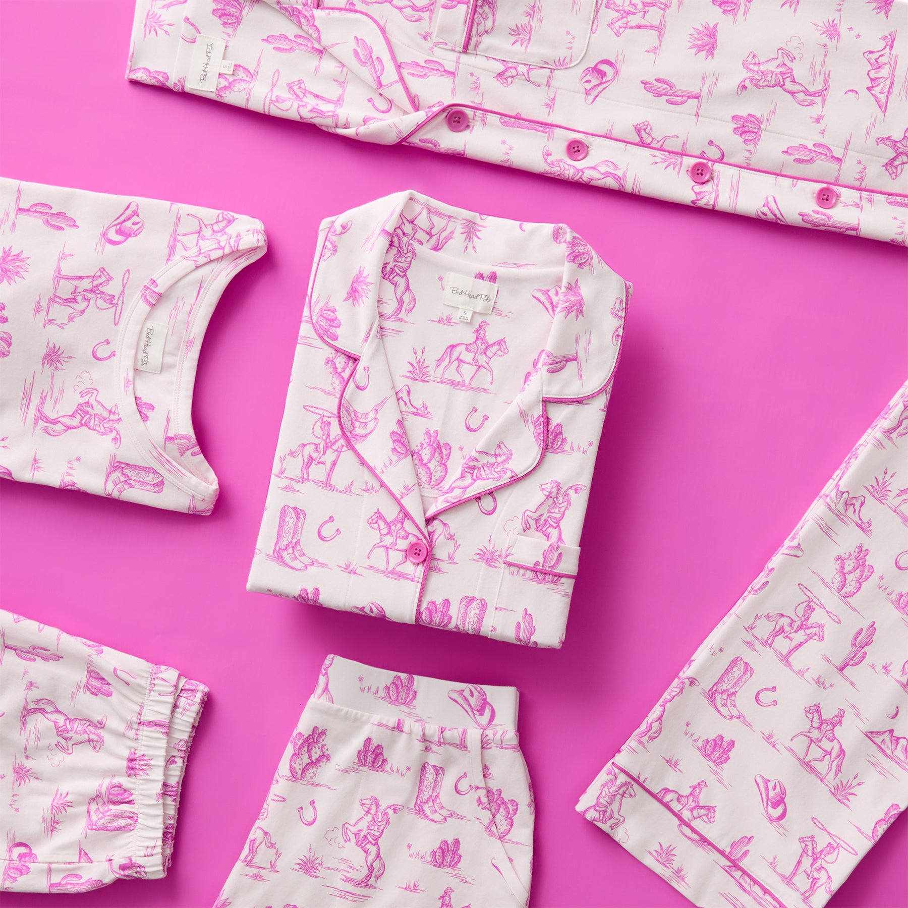 Folded and flat-lay pink Western toile-print cotton pyjama set with cowboy-themed illustrations on a pink background.