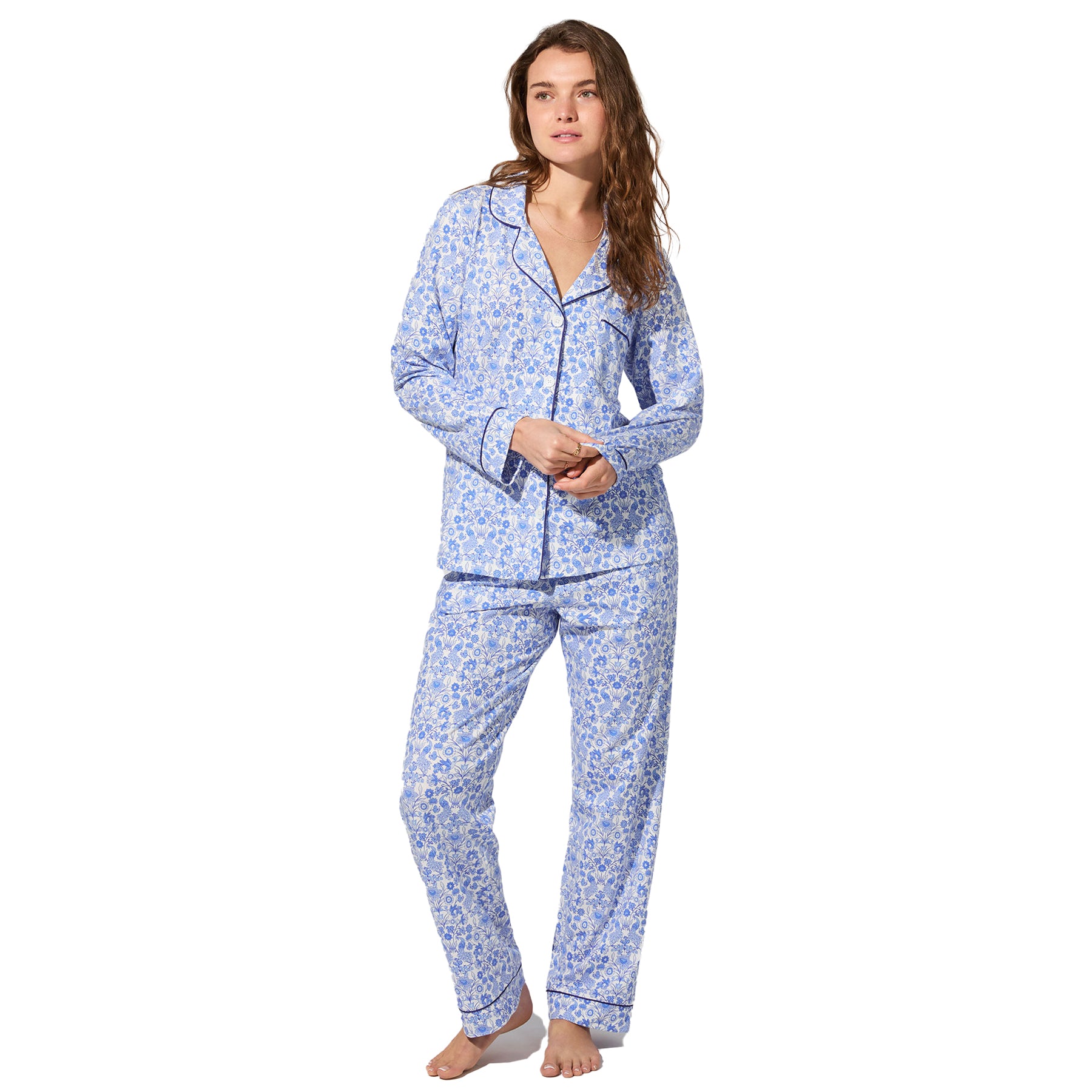 Full-length view of woman in white and blue floral pyjama set, long sleeve top and pants.