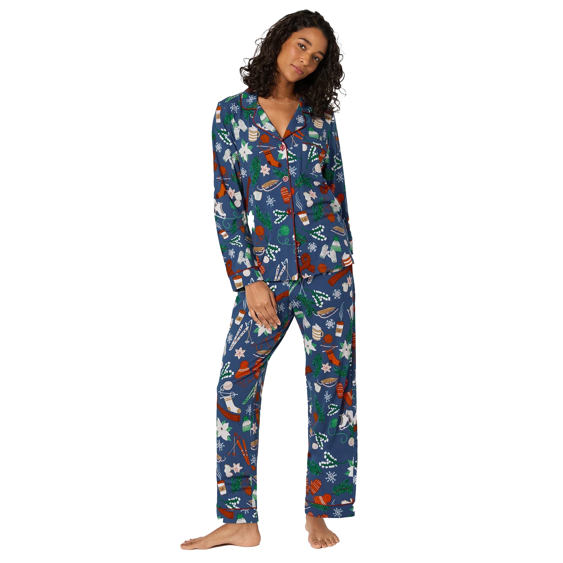 Woman wearing navy holiday pyjama set with festive print featuring snowflakes, mittens, and winter motifs, front view.