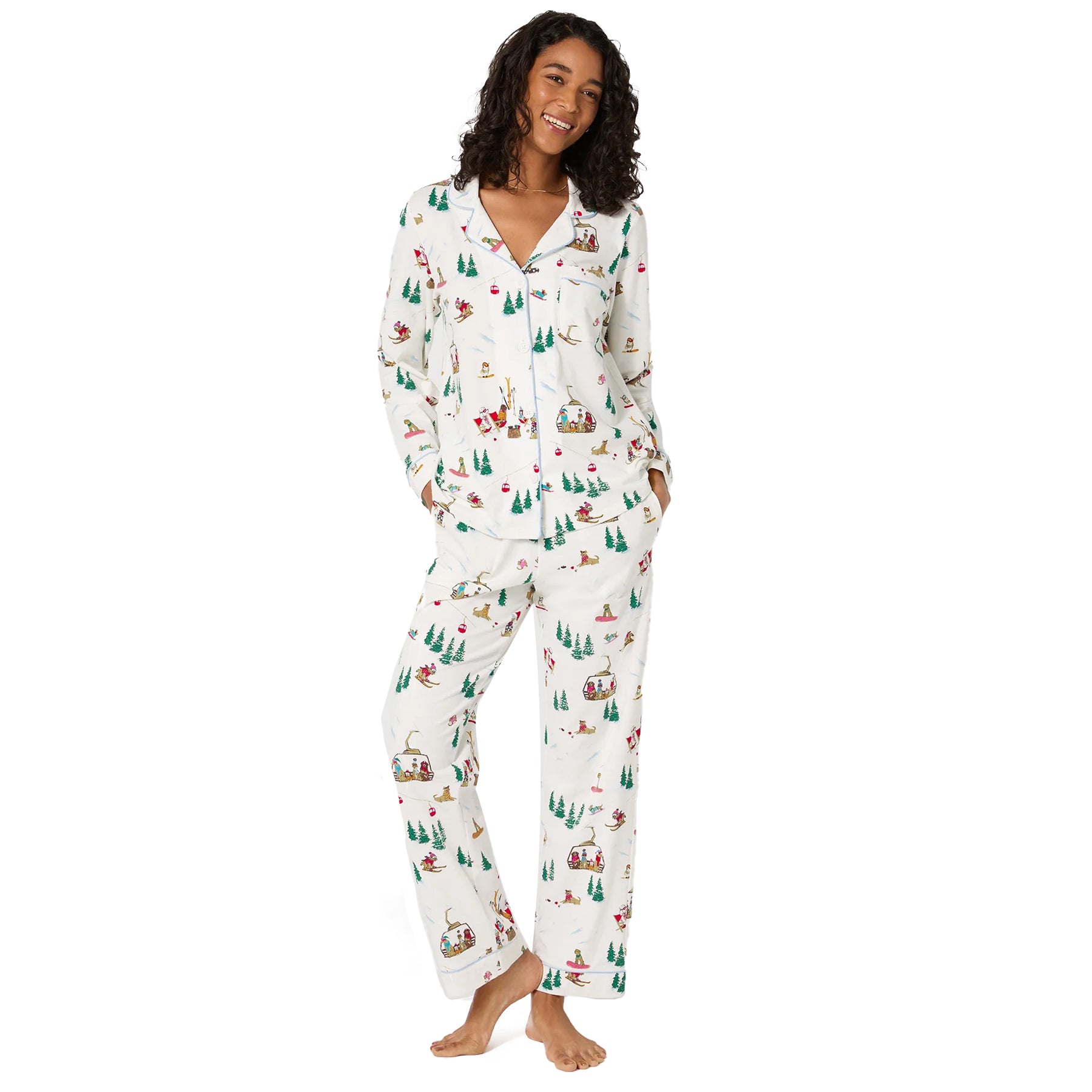 Woman wearing white holiday pyjama set with skiing dog and Christmas tree print, front view.