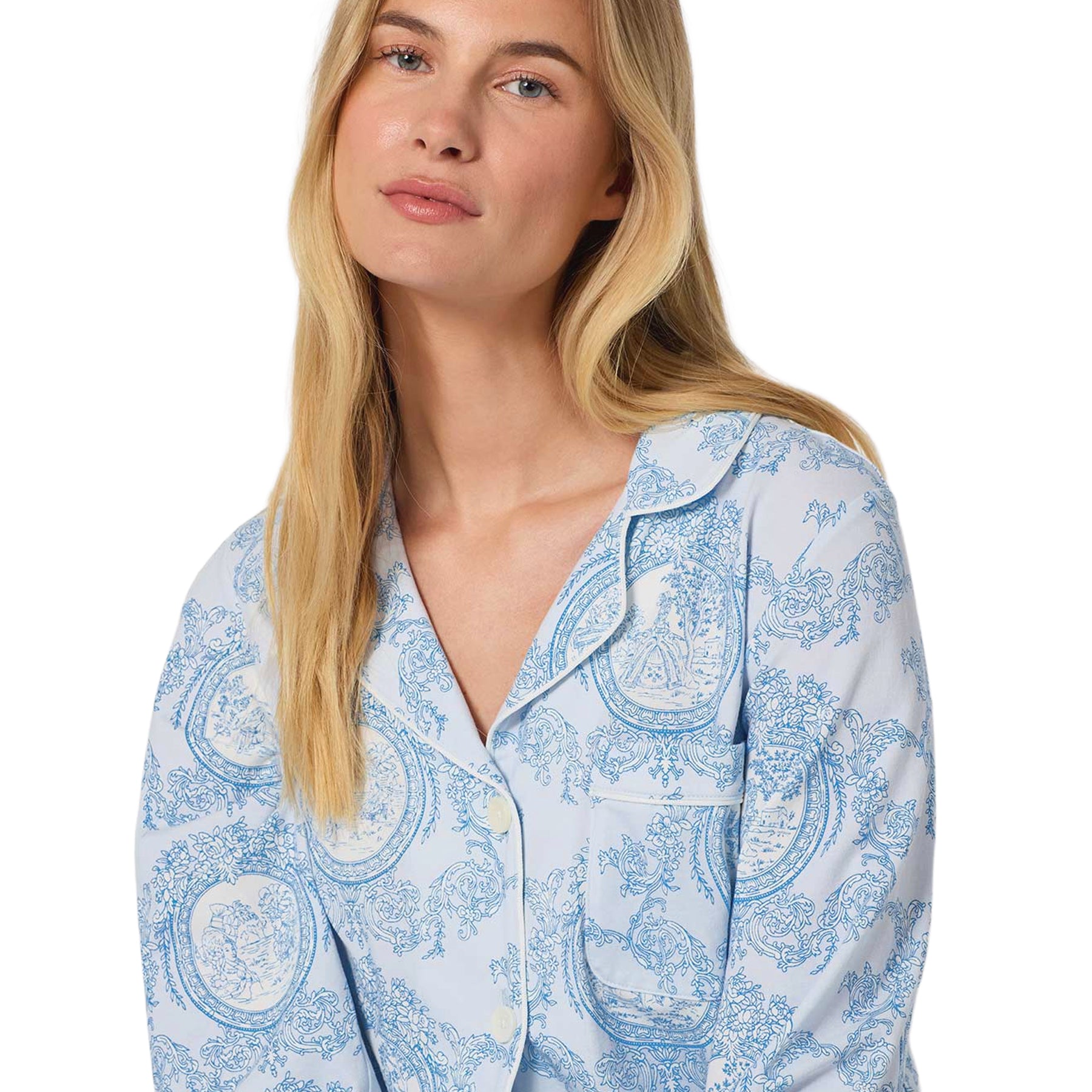 Close-up of a light blue pajama top featuring an intricate blue toile print, notched collar, button front and chest pocket.