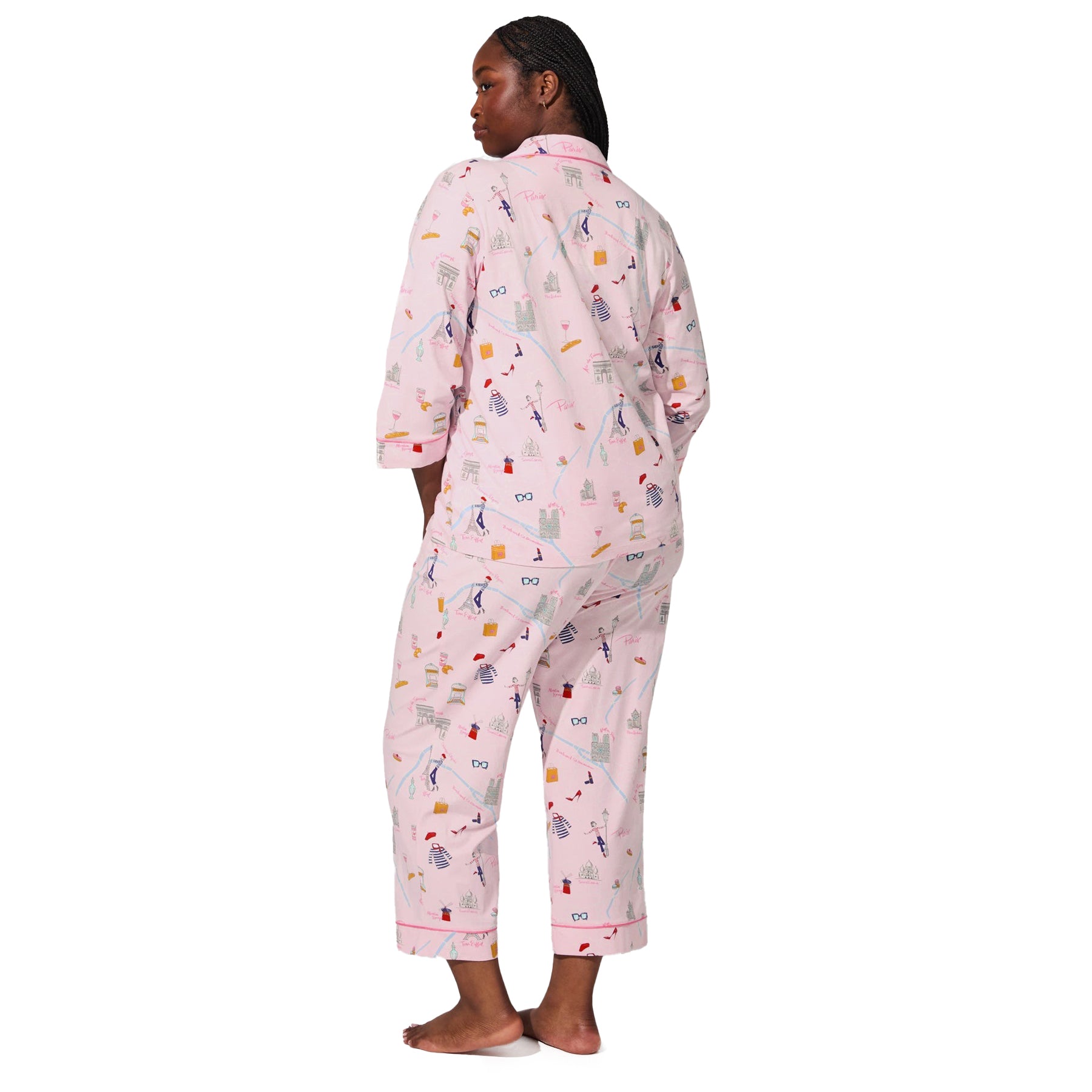 Back angled view of plus-size model wearing blush pink cropped pajama set with Paris-themed illustrations.