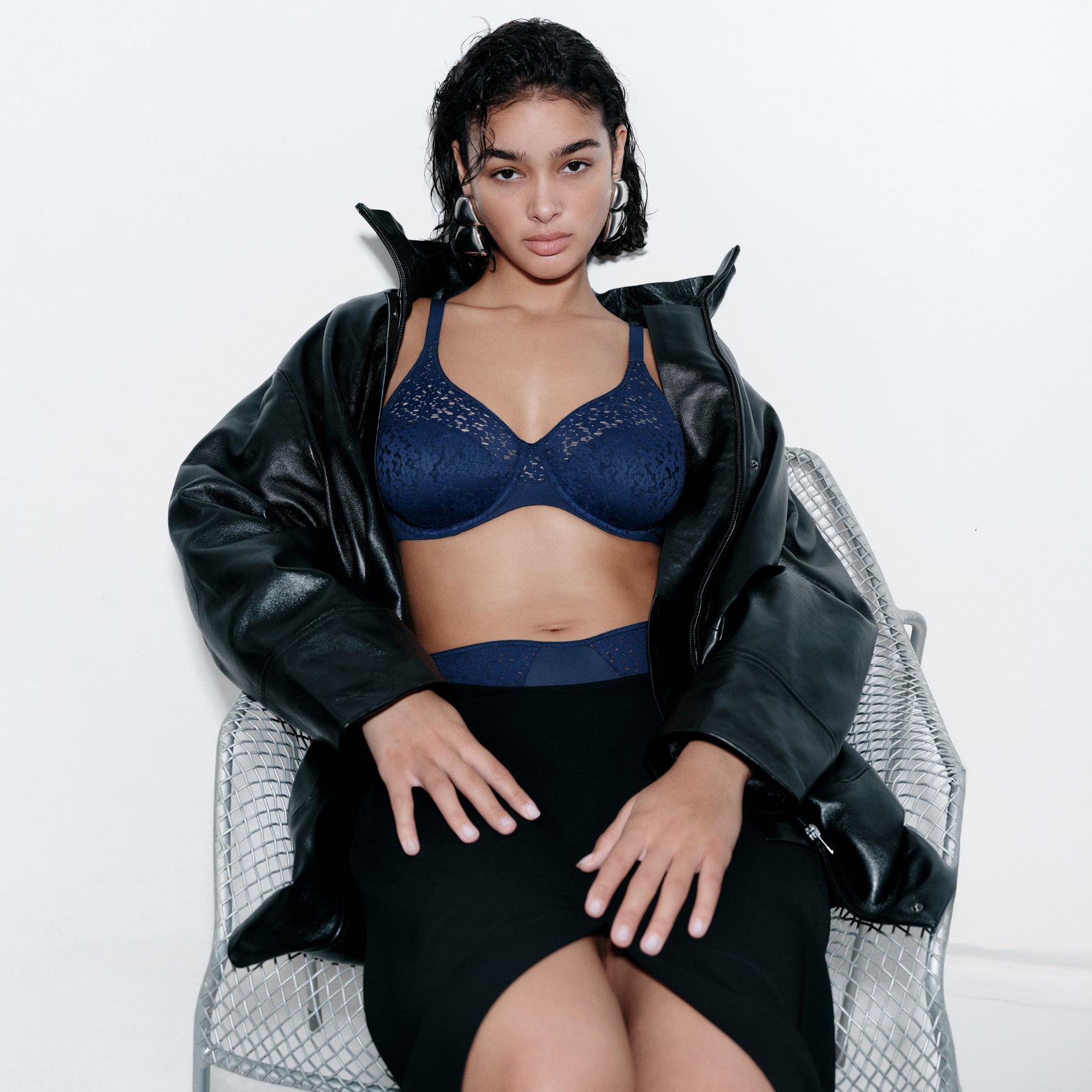 Model styled in navy lace bra and high-waisted briefs with leather jacket and black skirt.