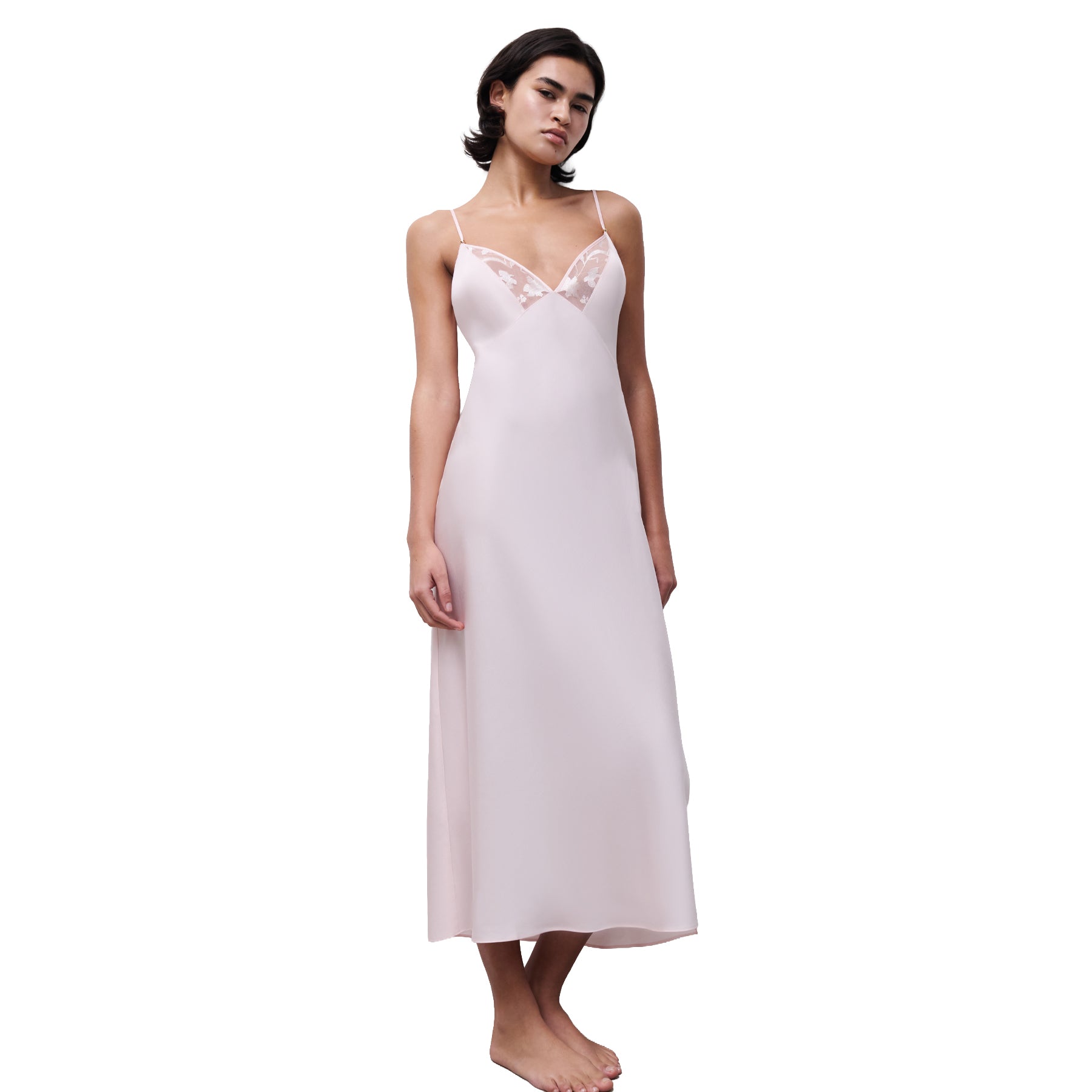 Blush pink long slip dress with delicate lace V-neck detail and adjustable straps, shown on model standing barefoot against a white background.