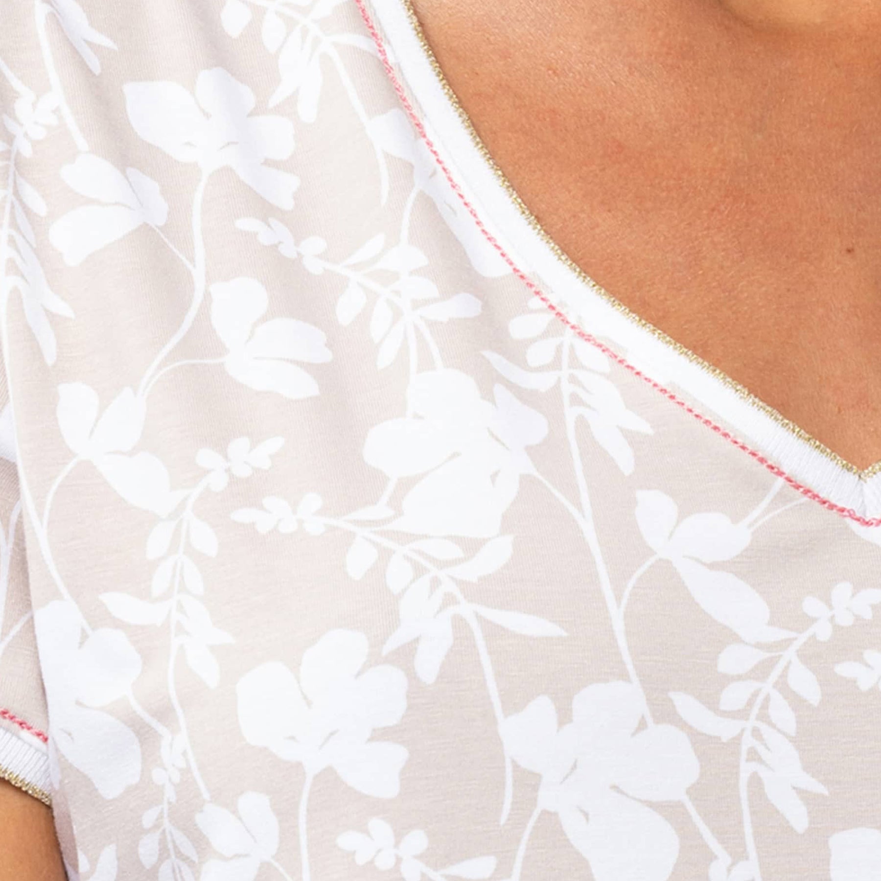 Close-up of white floral print on beige cotton nightdress with pink and gold neckline trim