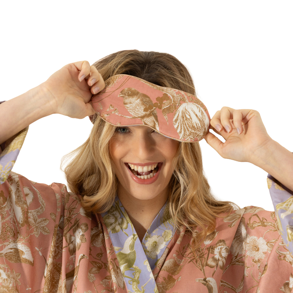 Woman wearing a dusty pink floral and bird print sleep mask with matching robe and lavender contrast trim.