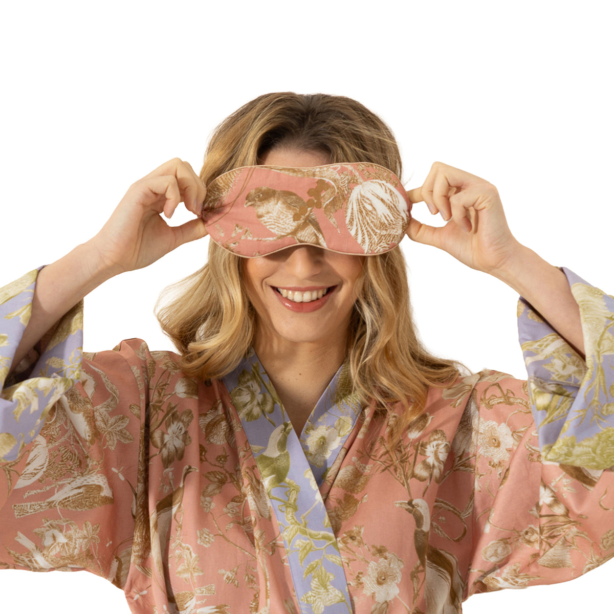 Woman modelling a dusty pink bird and botanical print sleep mask coordinated with a matching floral robe.