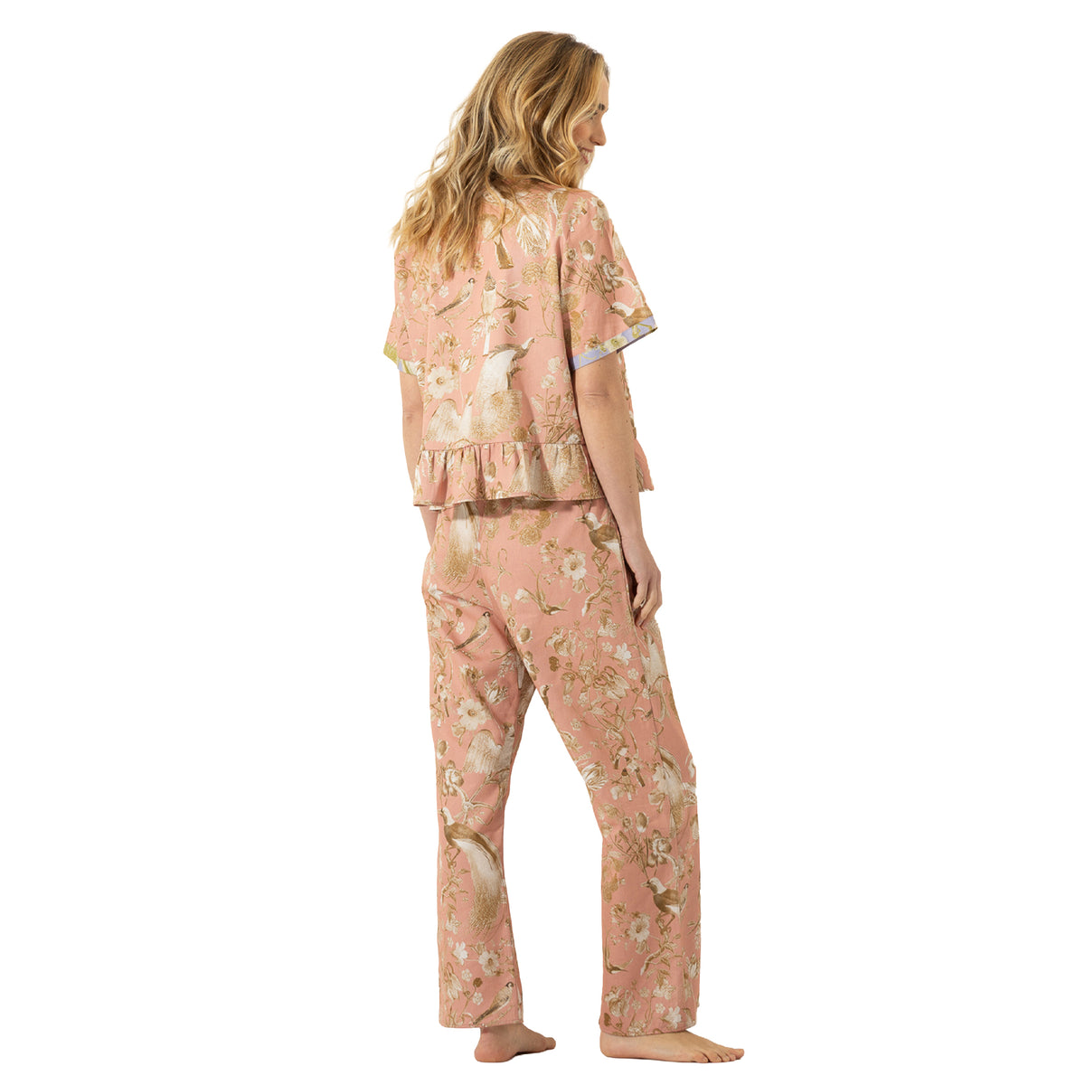 Woman modelling a dusty pink bird and floral print pajama set with short sleeves, relaxed pants and lavender contrast trim.