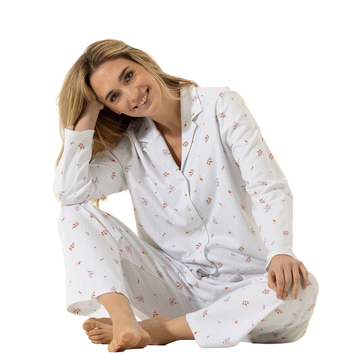 Woman seated comfortably wearing a white long-sleeve pajama set with delicate mini floral print, button-front top, and matching pants.