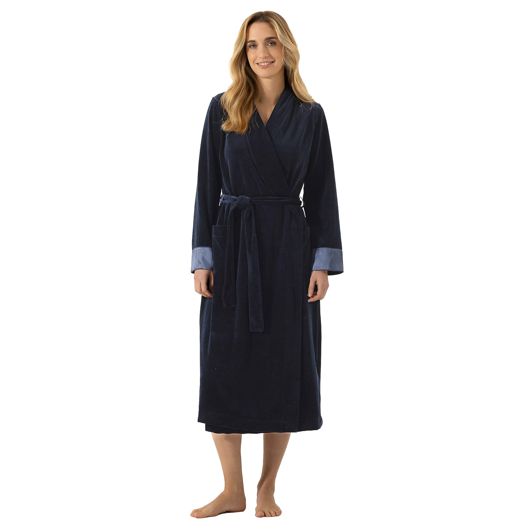 Woman wearing a long navy velour wrap robe with a shawl collar, matching tie belt, front pockets, and contrasting blue satin cuffs.