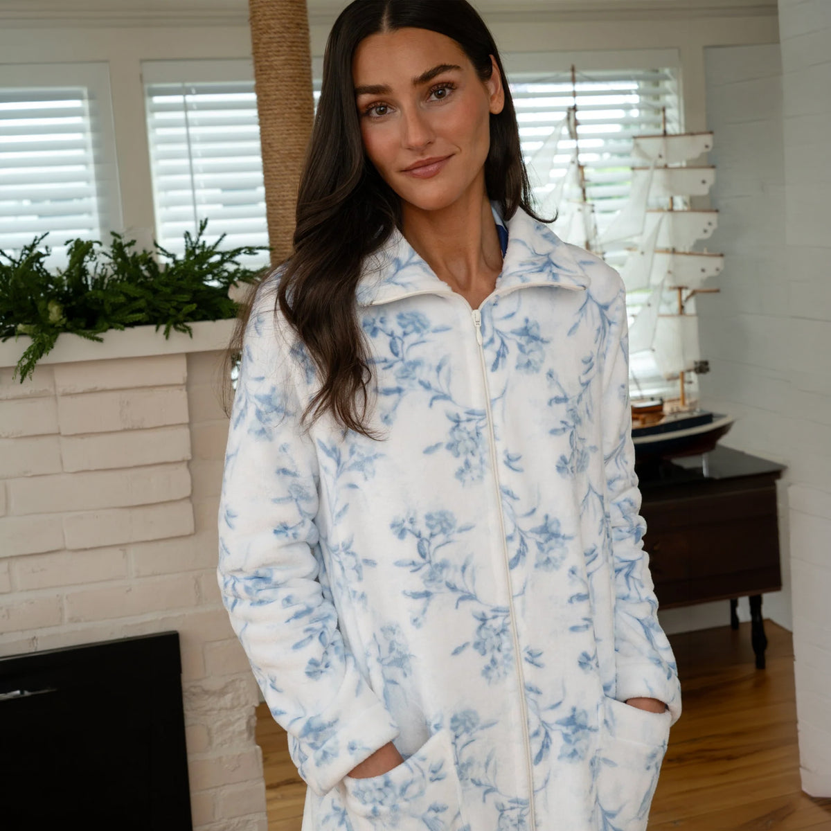 Woman wearing a soft white fleece zip robe with a delicate blue floral print, standing indoors with both hands in the front pockets.