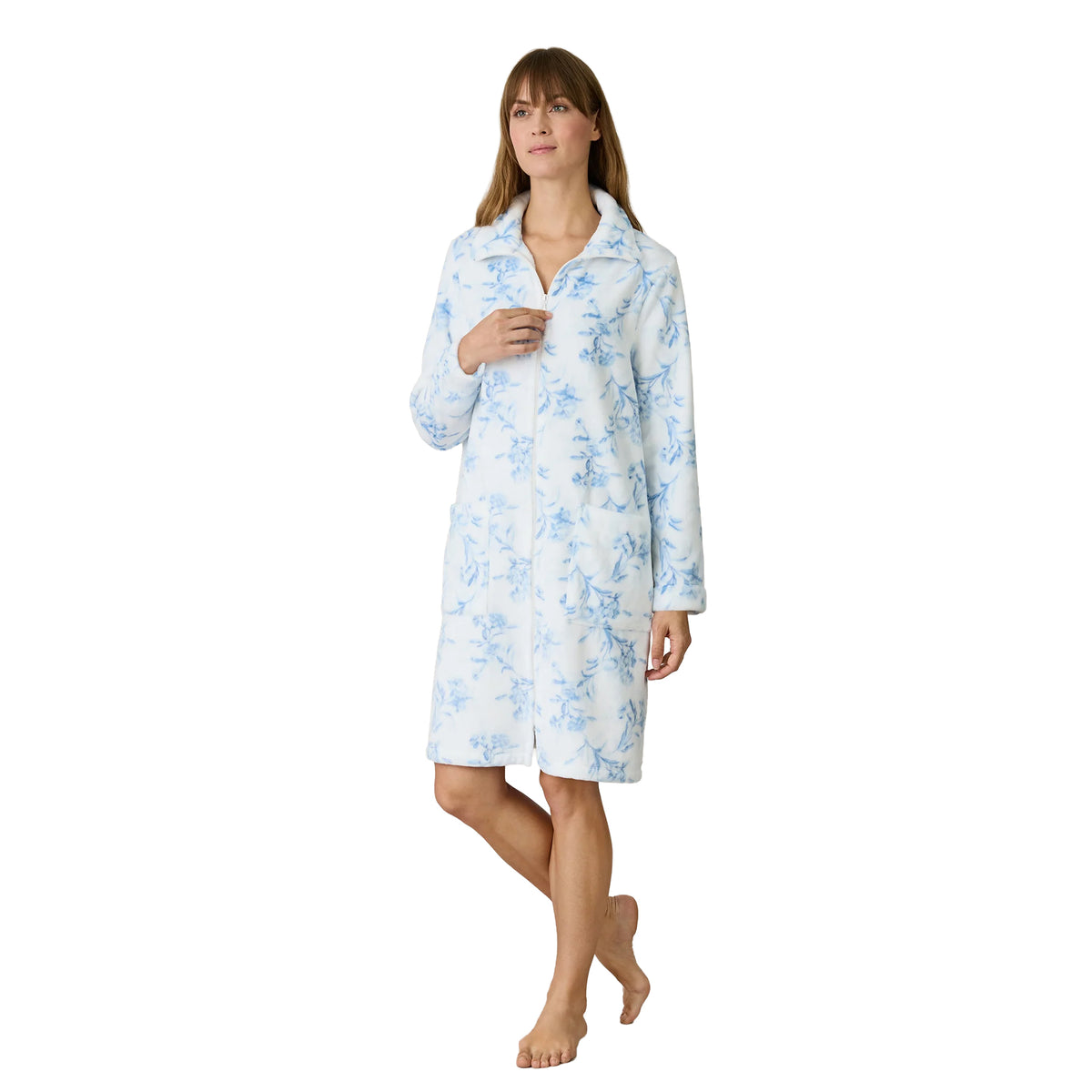Woman modelling a white fleece robe with a soft blue floral pattern, partially unzipped neckline, long sleeves and two spacious front pockets.