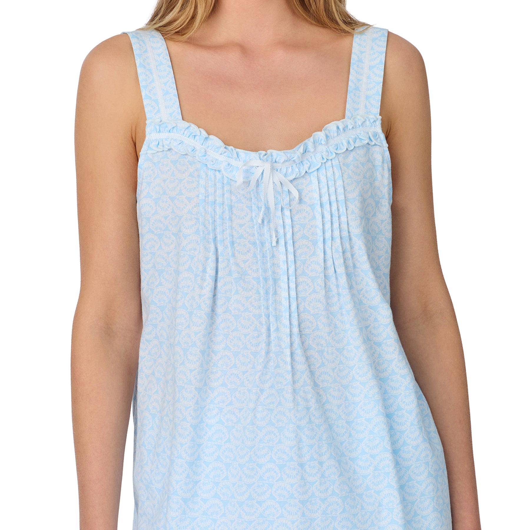 Woman wearing a sleeveless light blue pajama top with delicate ruffle trim and a bow detail at the neckline.