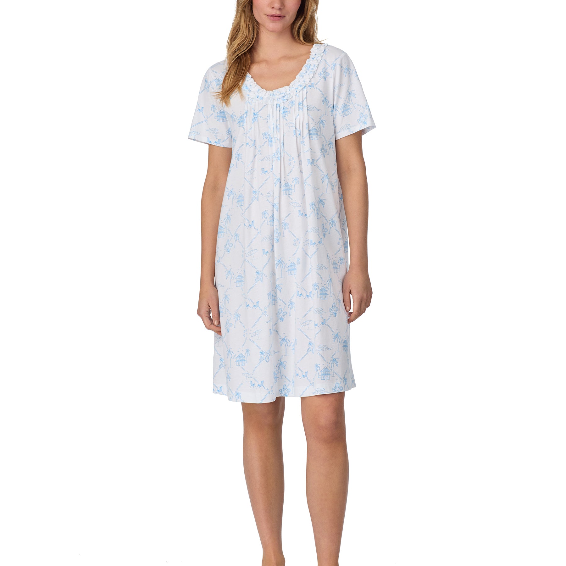 Woman wearing a short-sleeve white nightgown with a soft blue tropical print, featuring a ruffled neckline and above-the-knee length.