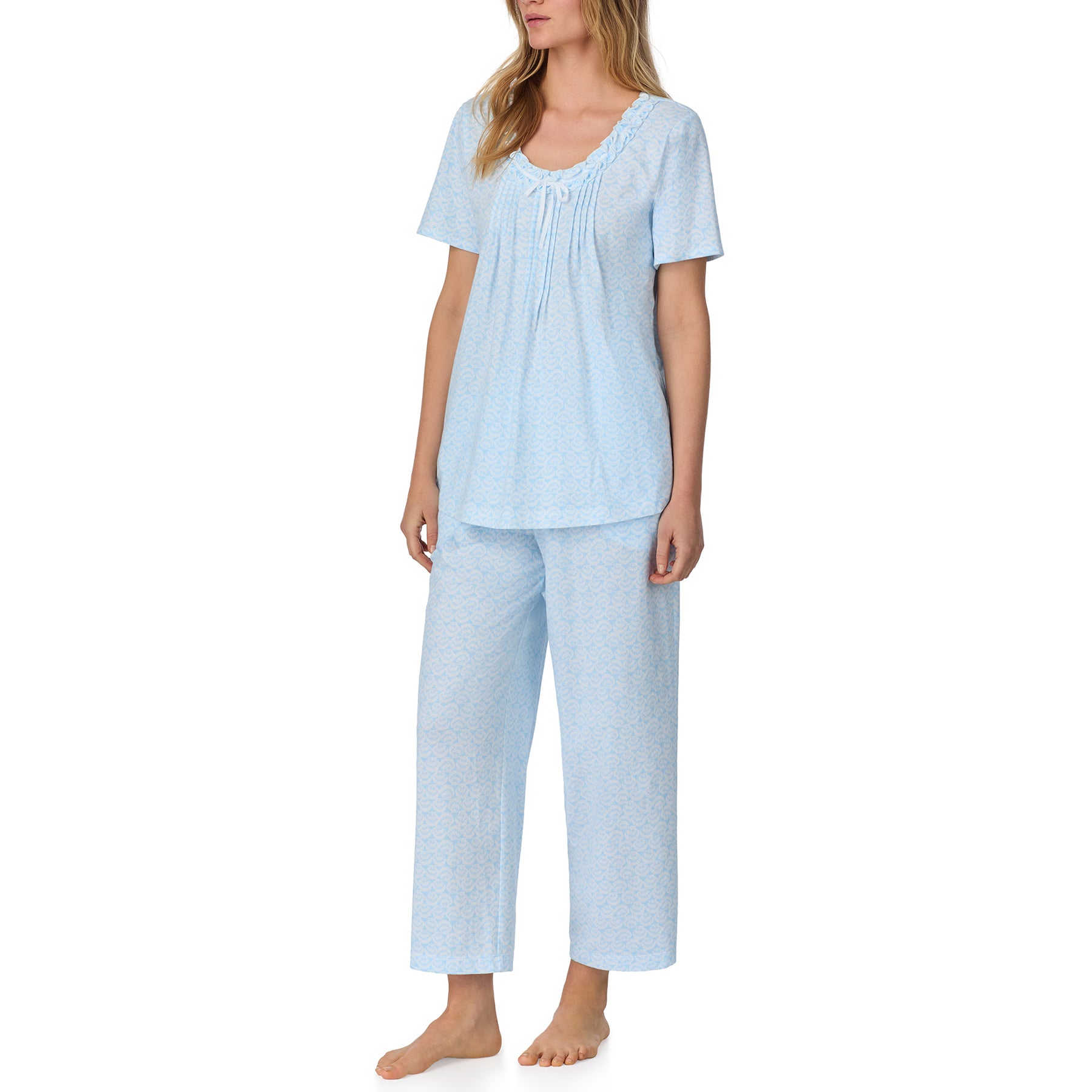 Woman wearing a light blue short-sleeve pajama set with a delicate all-over print and gathered neckline detail, standing against a white background.