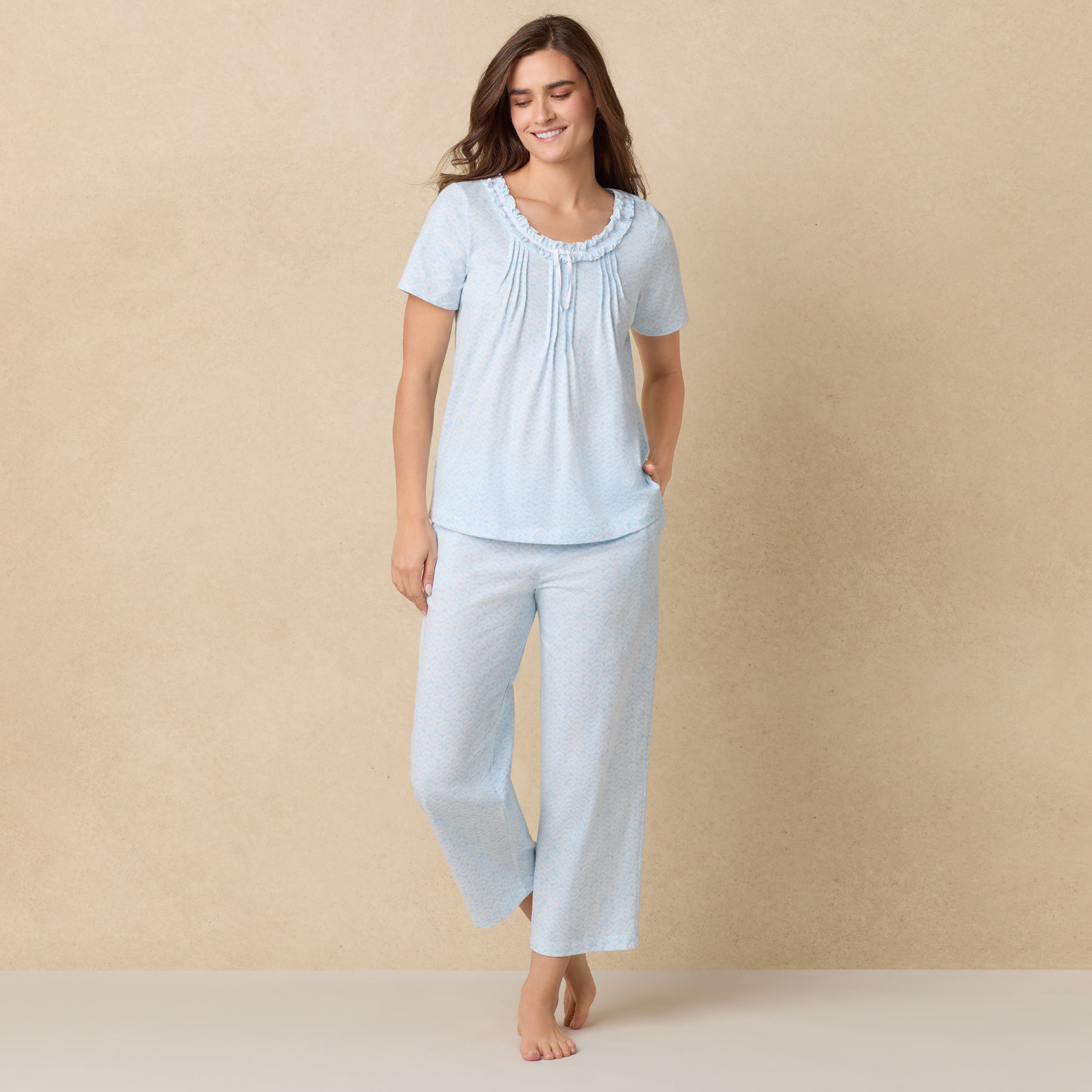 Smiling woman wearing the same blue pajama set, posing with one leg forward against a soft beige backdrop.