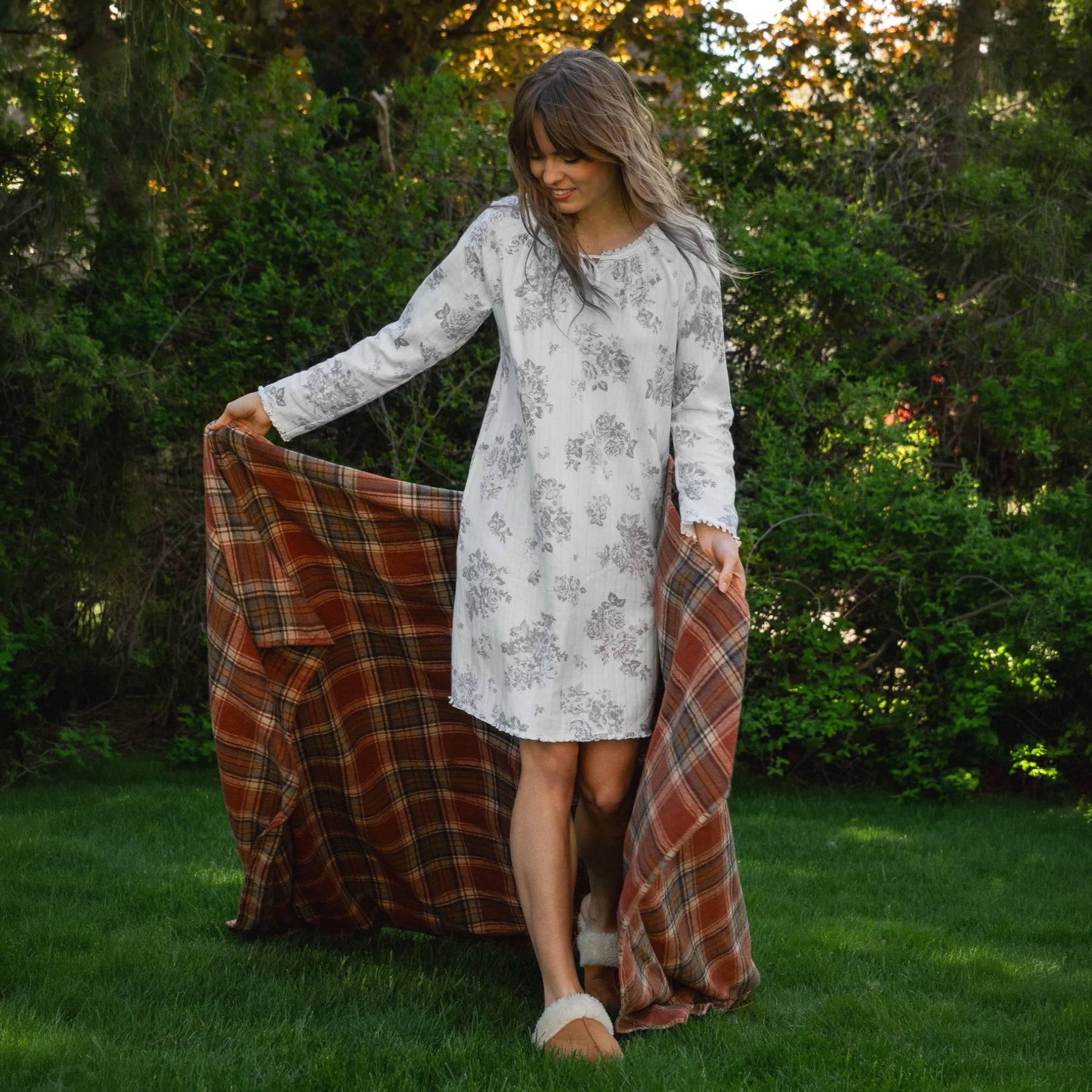 Woman outdoors wearing a white long-sleeve sleep gown with a delicate grey floral print and relaxed knee-length silhouette.