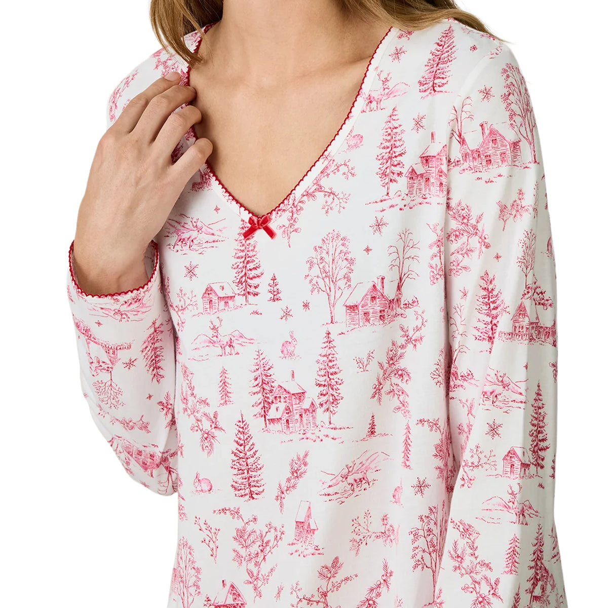 Close-up of Carole Hochman chemise featuring a delicate pink winter toile print with cottages, pine trees, deer and snowflakes, finished with red scalloped neckline trim and a small satin bow.