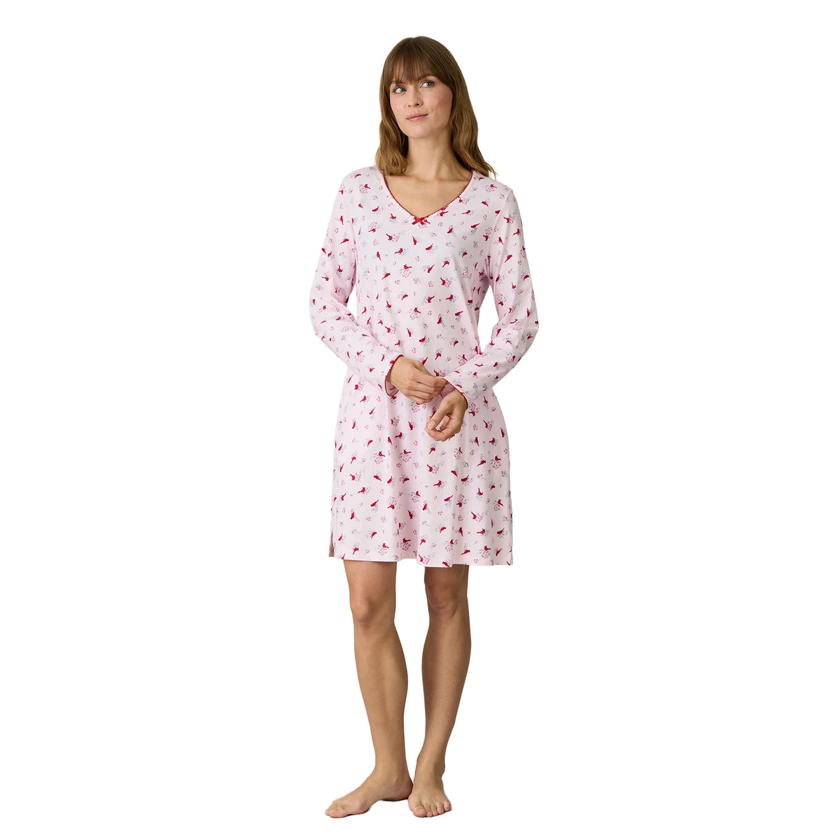Woman wearing a Carole Hochman light pink long-sleeve chemise featuring an all-over red cardinal bird and grey botanical print, a V-neckline with red scalloped trim and a small red bow.