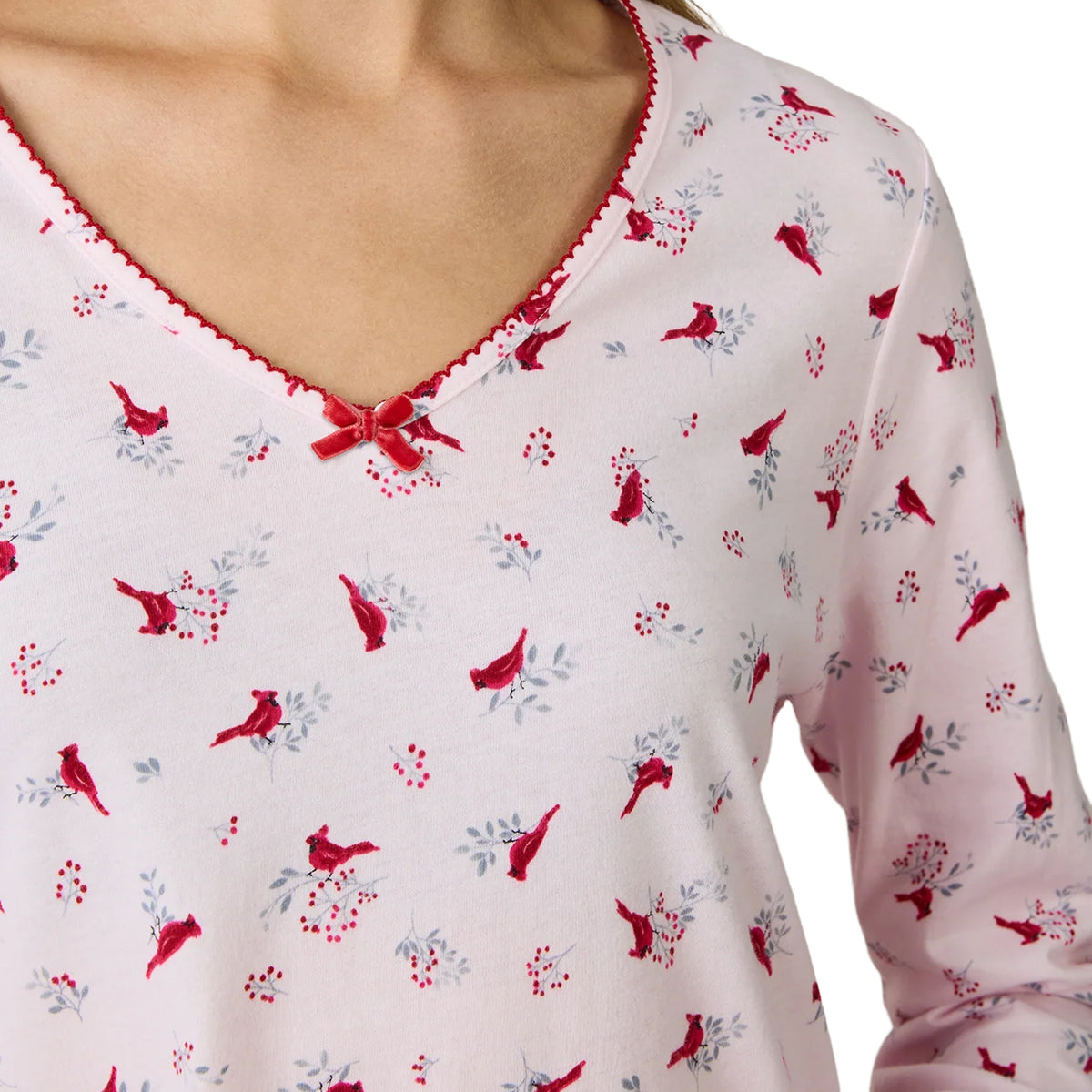 Close-up of a Carole Hochman chemise showing red cardinal birds, grey branches and red berries on pale pink fabric, with delicate red scalloped neckline trim and a satin bow.