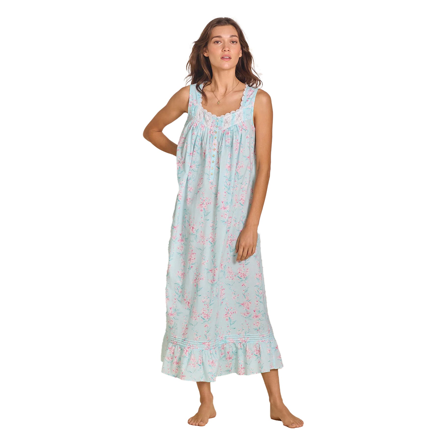 A woman wearing a sleeveless, light blue floral print maxi nightgown with lace-trimmed straps and a ruffled hem, standing barefoot in a relaxed pose.