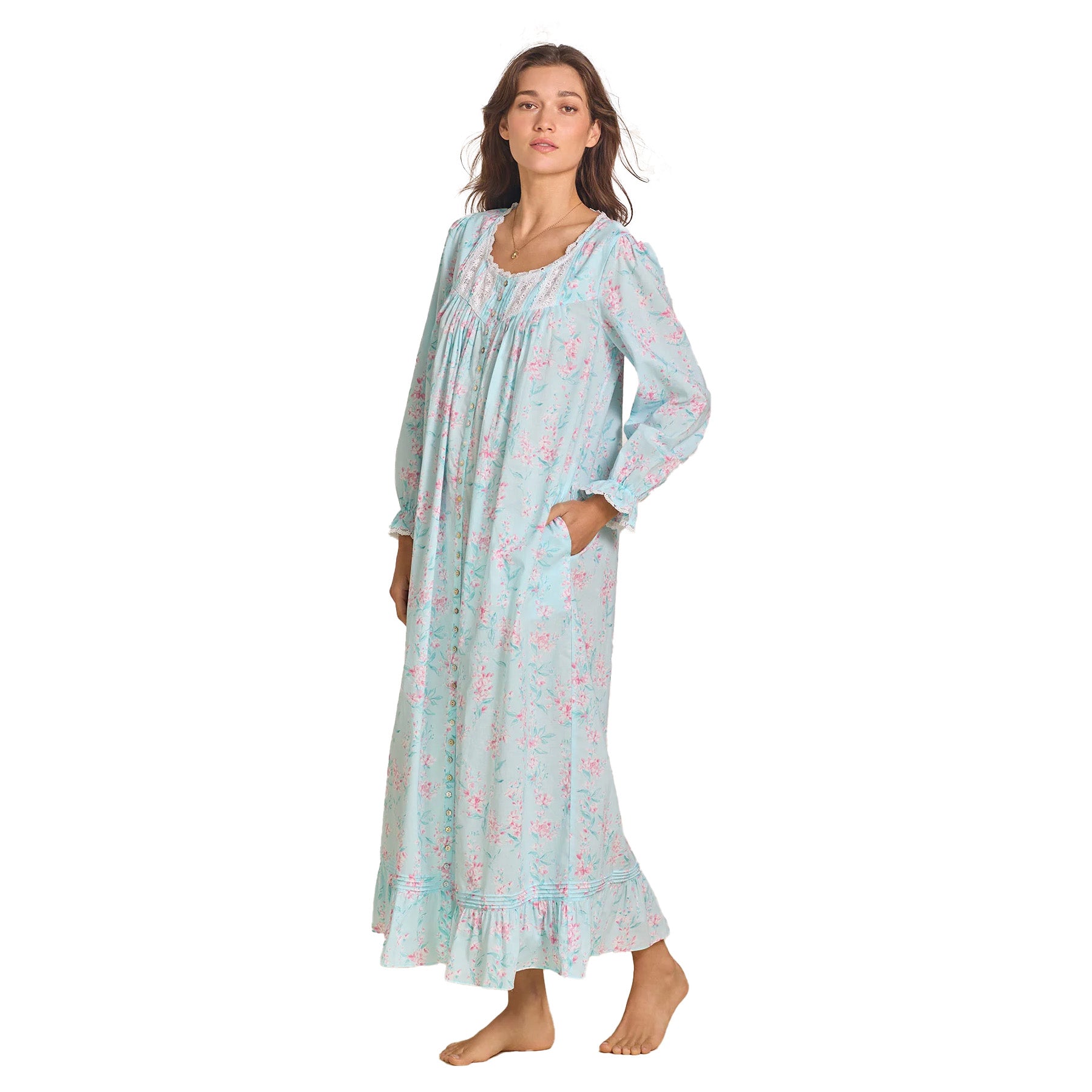 A woman wearing a long-sleeved, light blue floral print maxi nightgown with lace-trimmed neckline, ruffled cuffs, and a flowing silhouette.