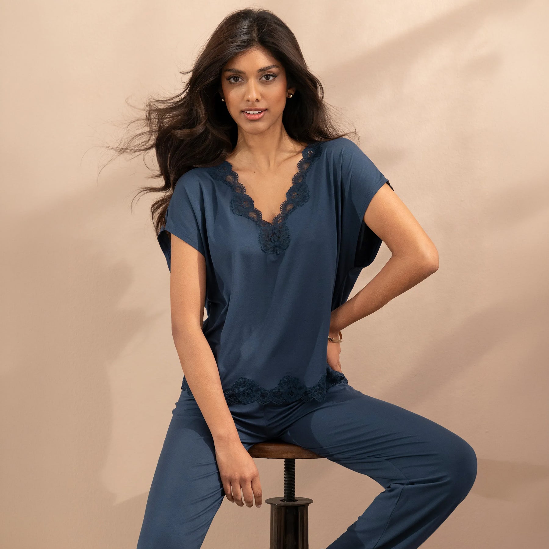 Woman modelling a dark teal pajama set with a relaxed lace-trimmed top and coordinating long pants.
