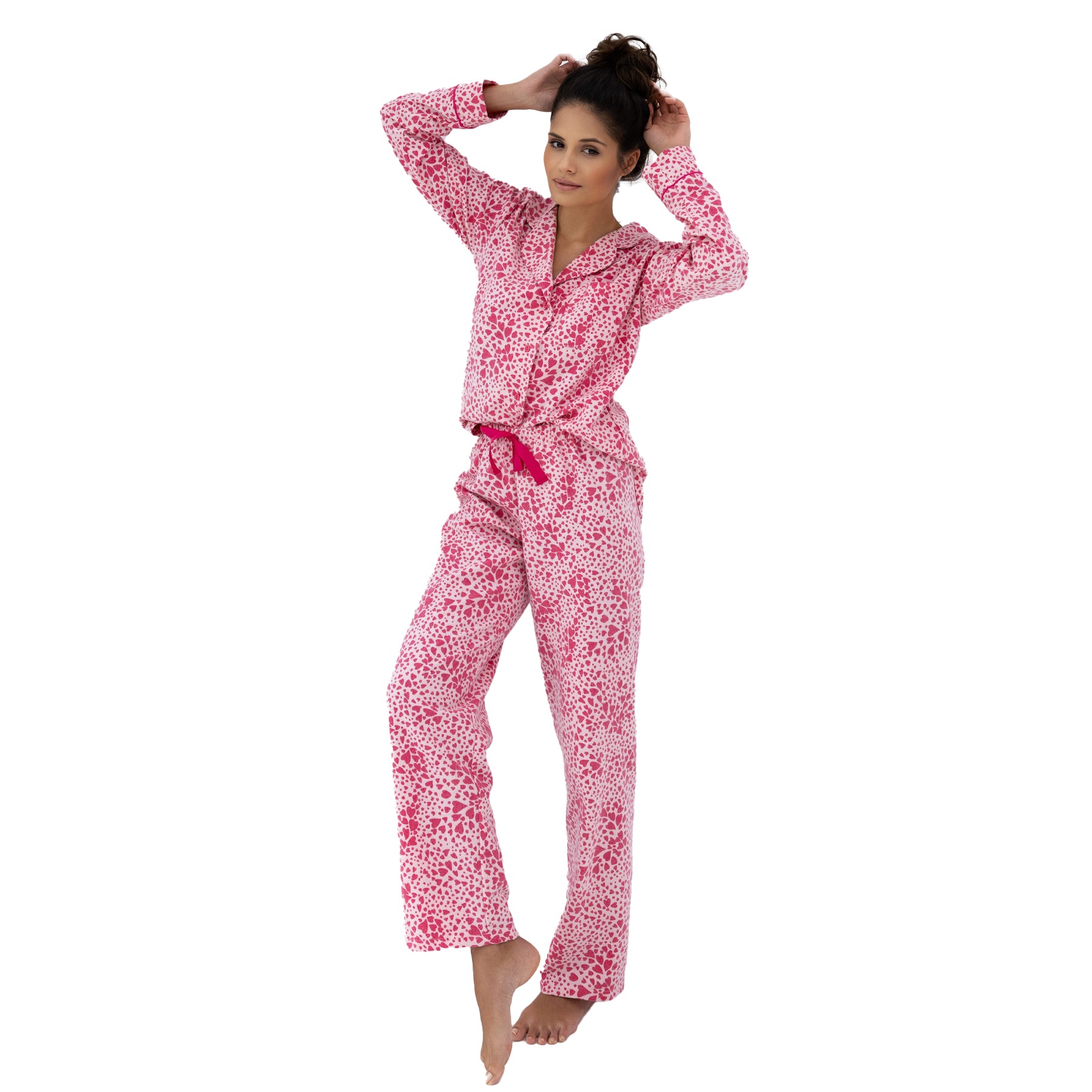 Woman posing playfully in full-length pink heart-print pyjama set with long sleeves and matching pants.