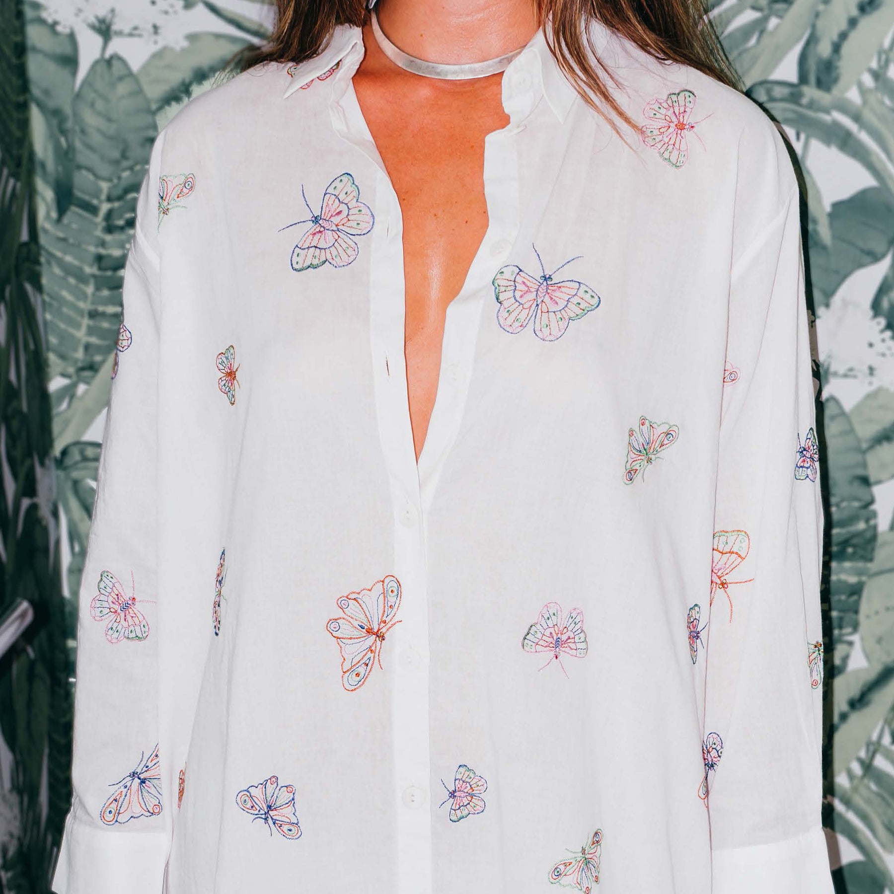 Long sleeve white button up collared shirt dress with multicoloured embroidered butterflies throughout. Front view close up on model.