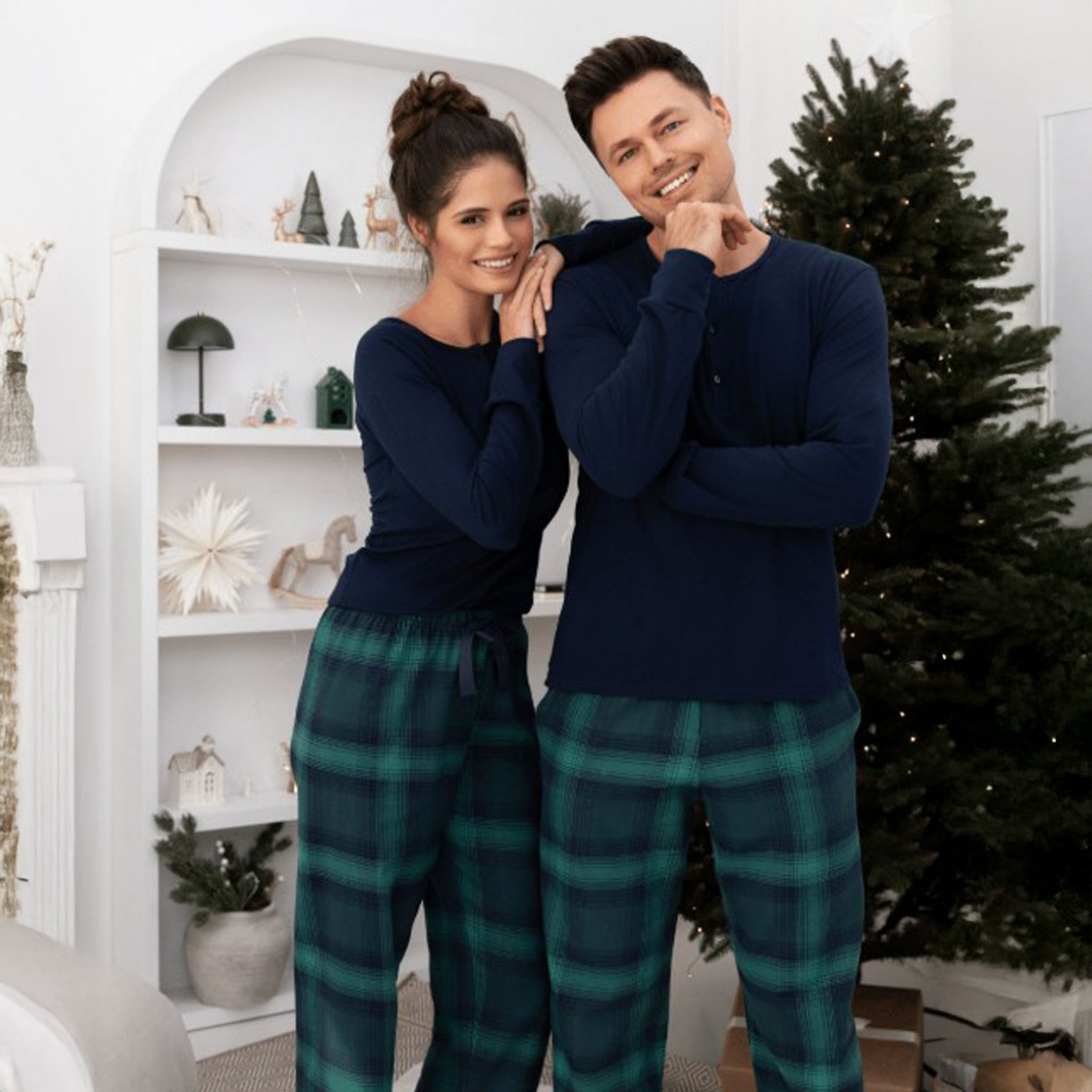 Man and woman wearing matching navy and green plaid pajama sets, cozy holiday loungewear