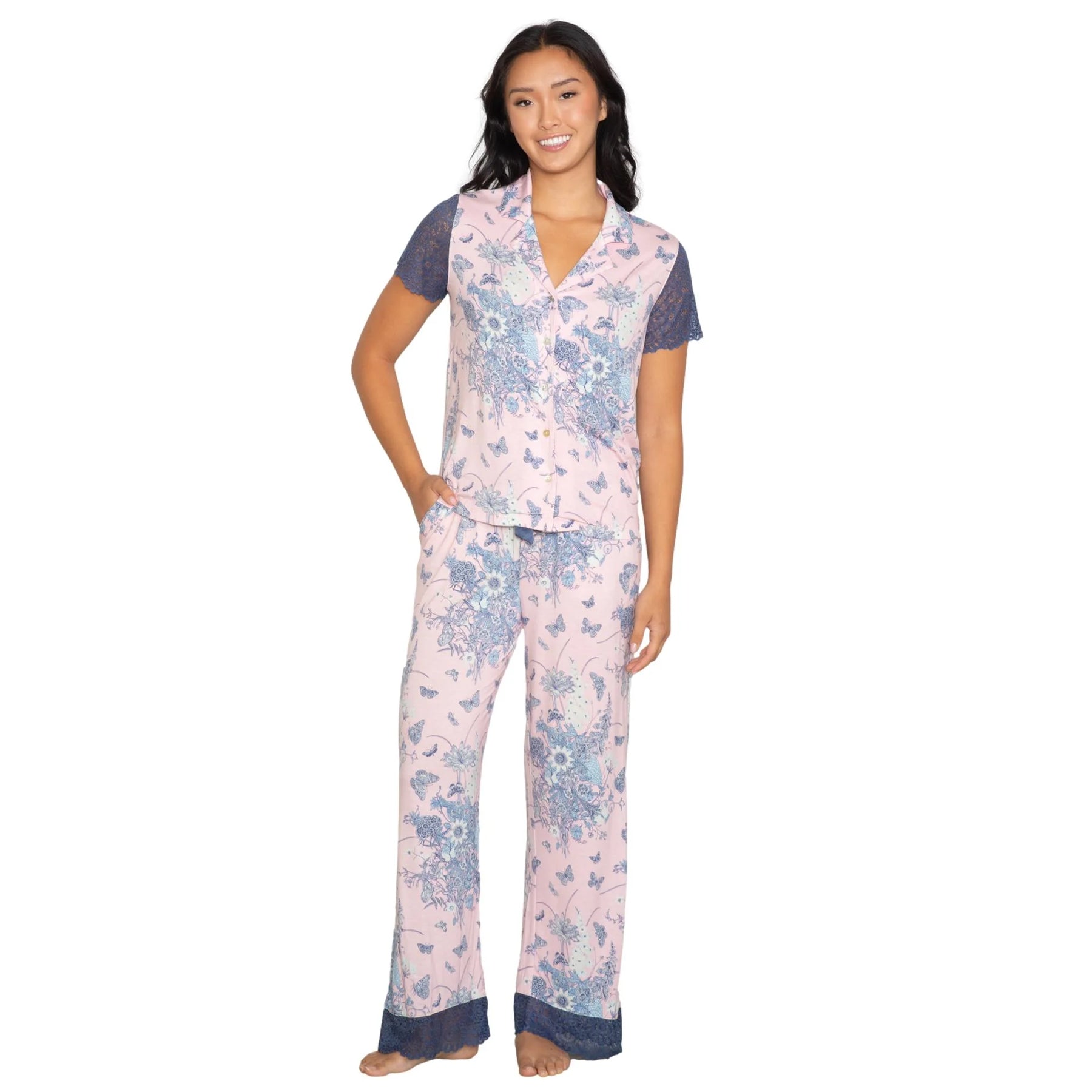 Woman wearing a soft pink floral pajama set with blue lace sleeve detail and trim, short sleeve button-front top and relaxed pants