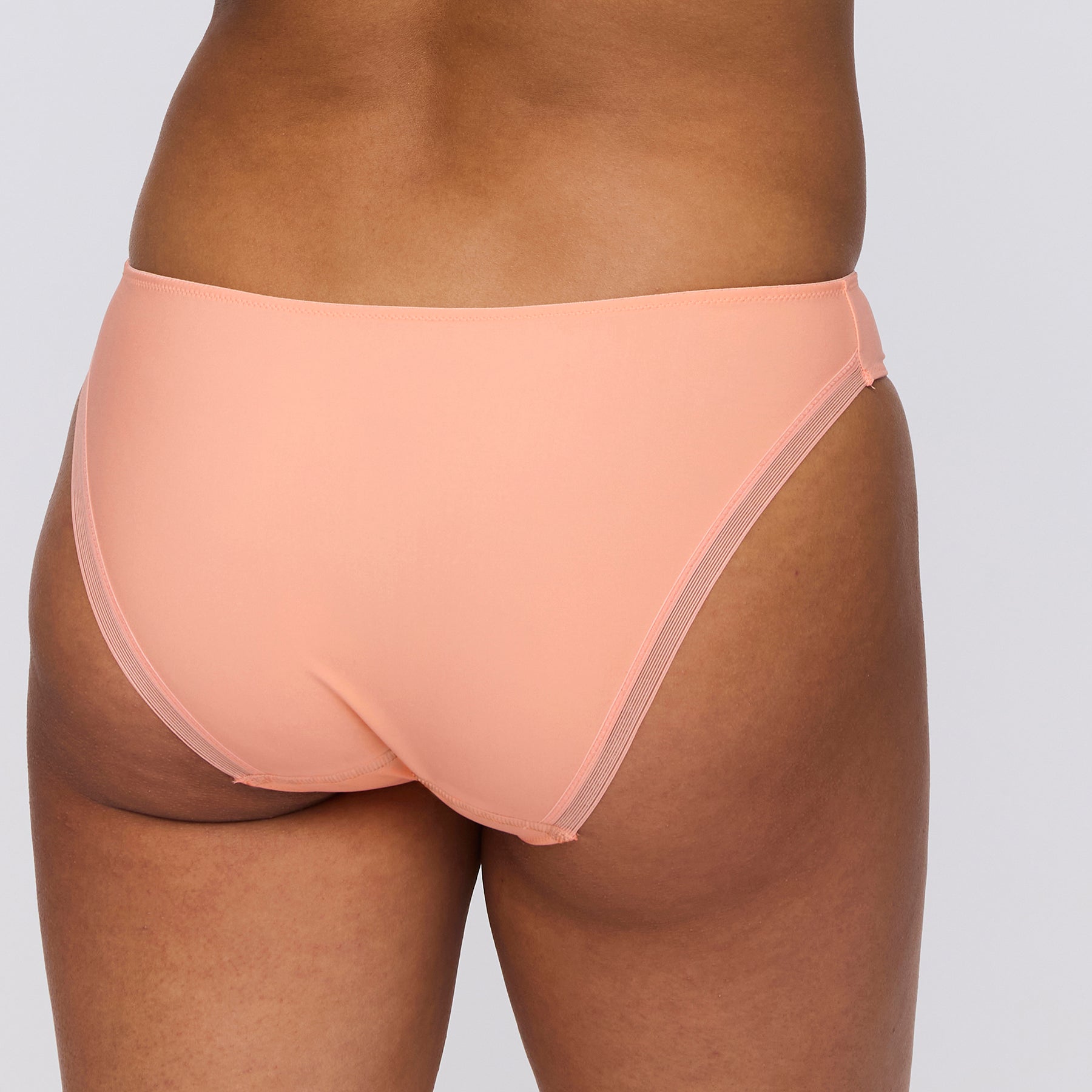 Seamless rio bikini brief in papaya smoothie light orange. Rear view close up on model. 