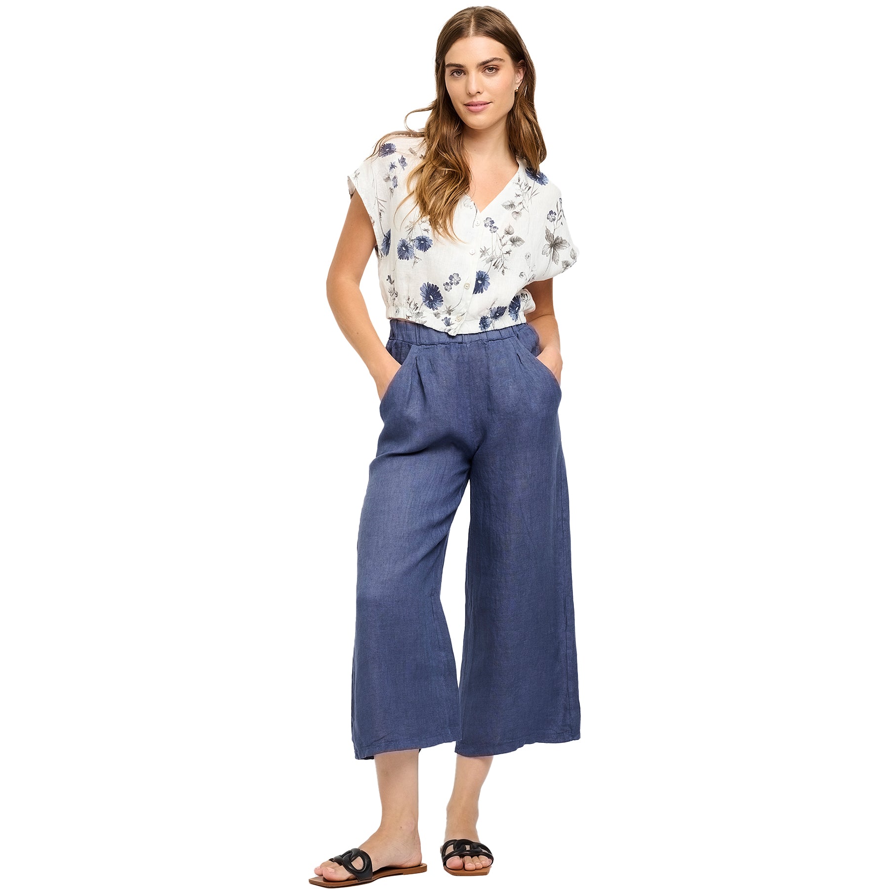 Woman wearing a white floral blouse and deep sea blue cropped linen pants with side pockets - lightweight summer outfit.