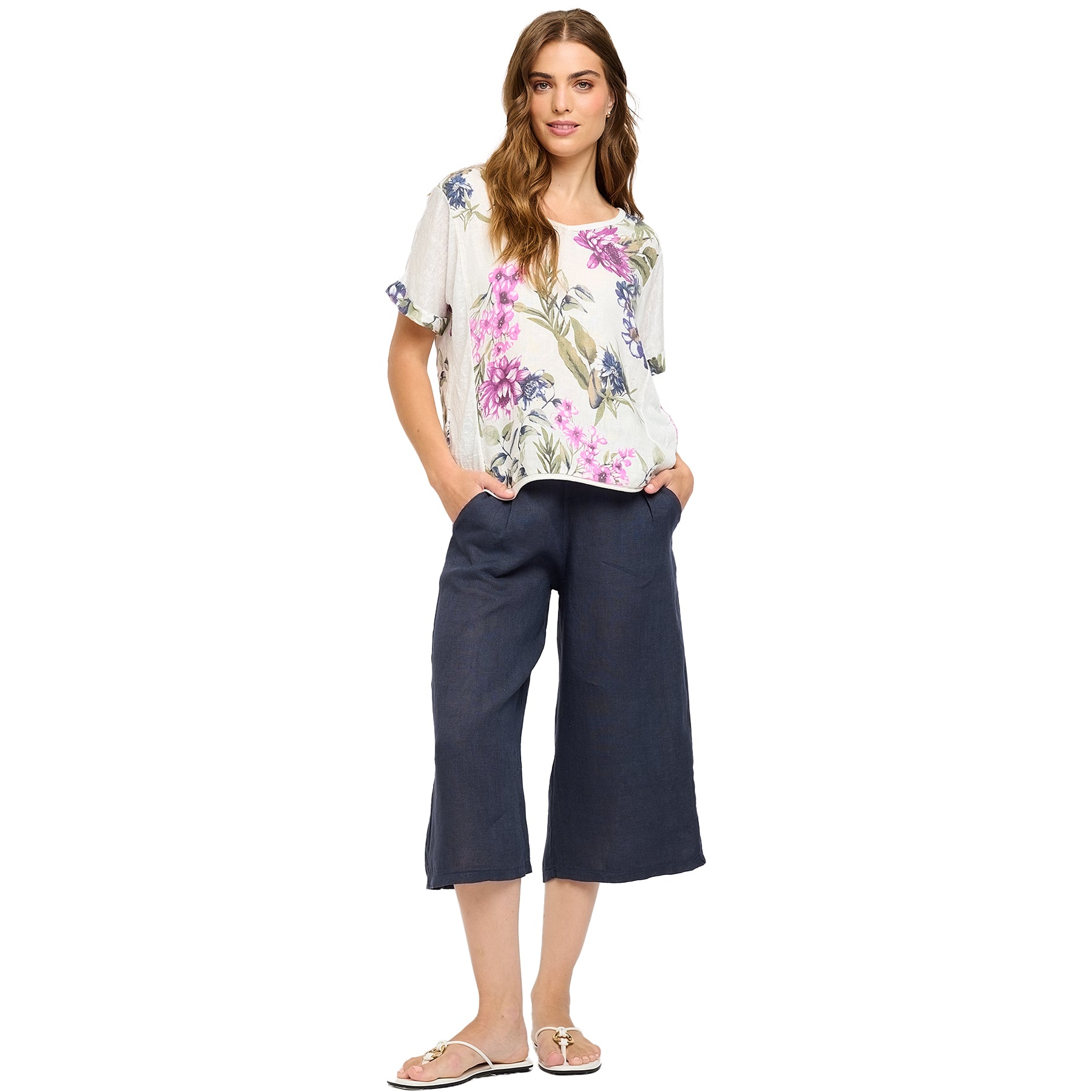 Full view of woman in a floral linen blend top with rolled sleeves, paired with navy culotte pants and sandals - relaxed summer outfit.
