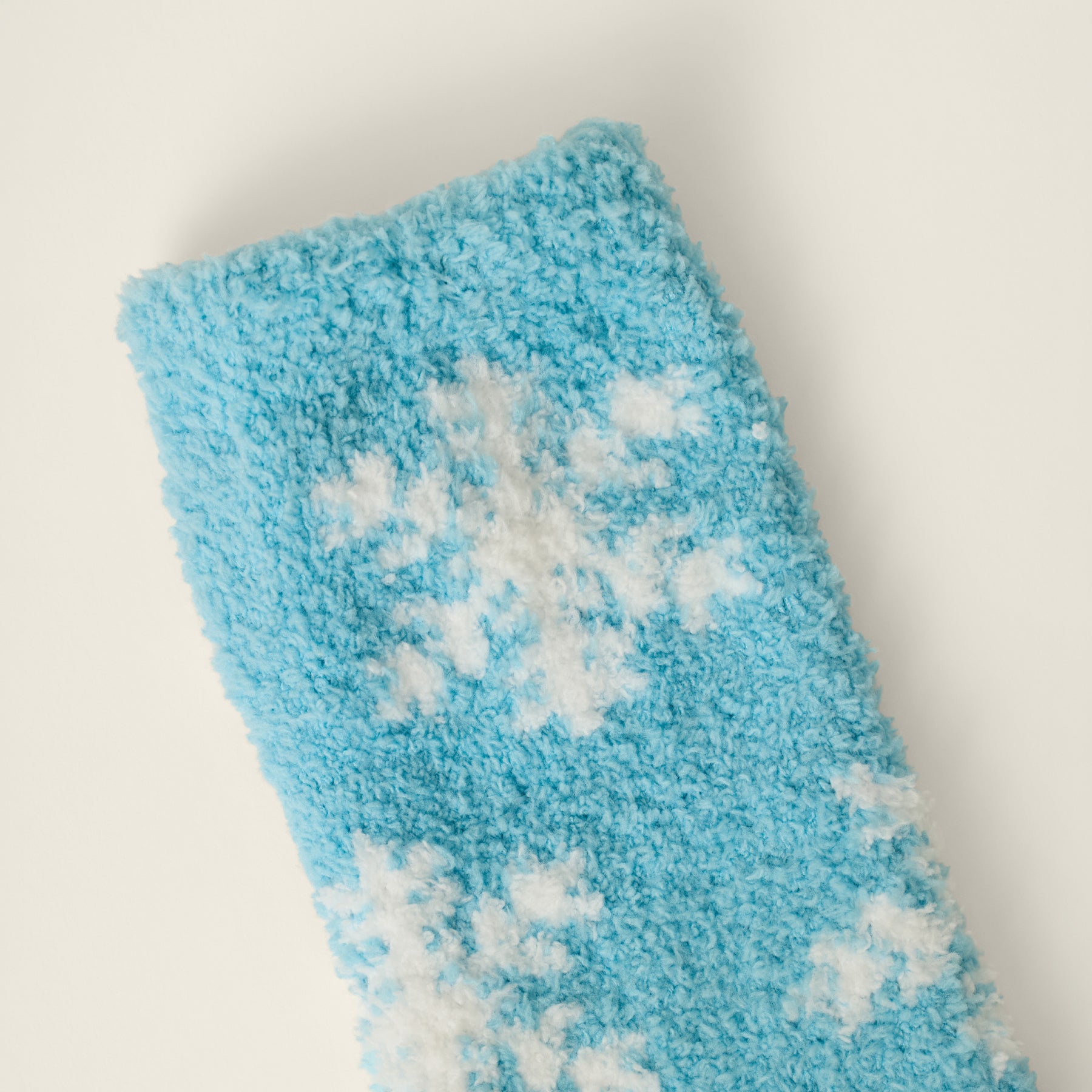 Close-up of soft blue plush sock fabric featuring a white knitted snowflake pattern.