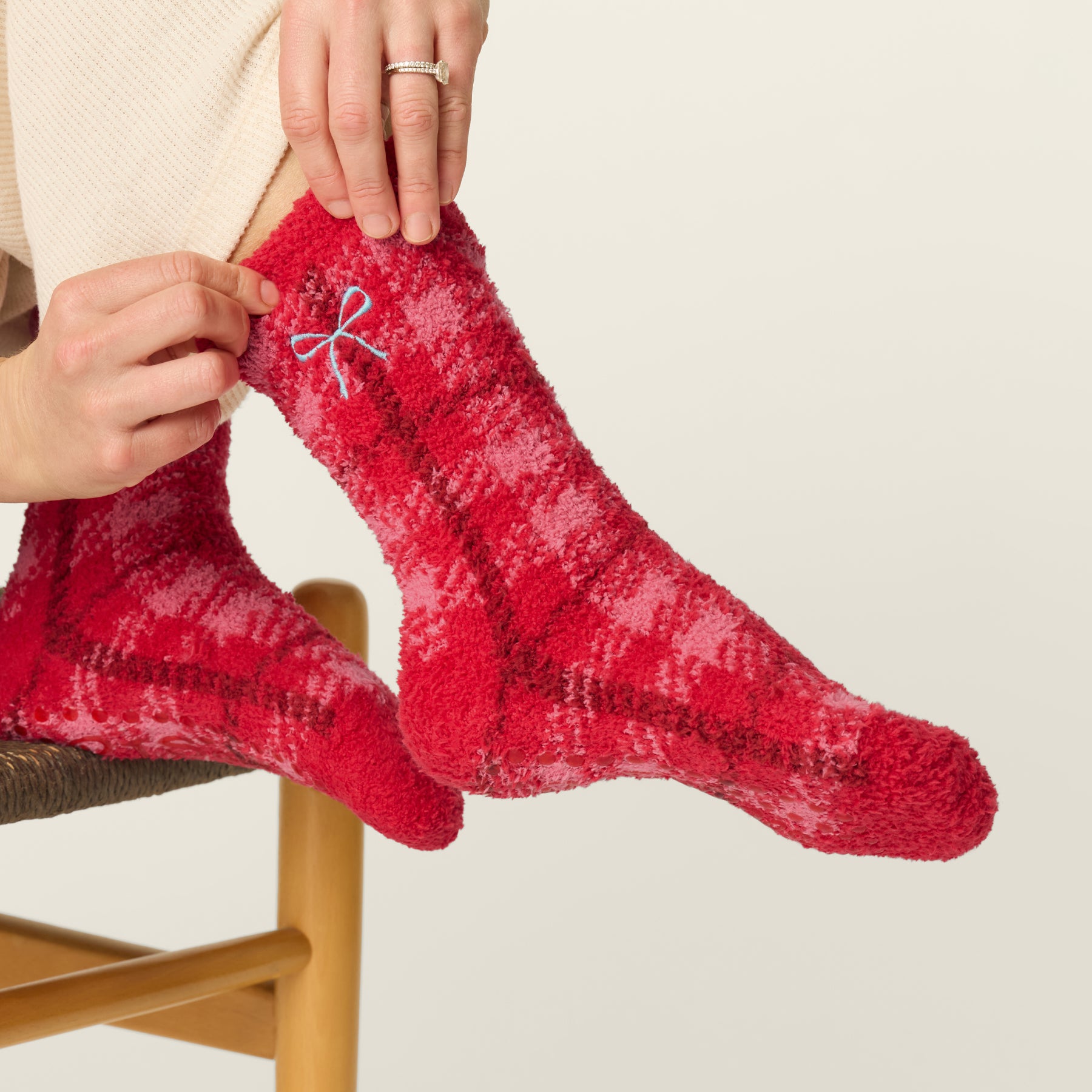 Side view of red plaid fuzzy socks with blue embroidered bow detail and non-slip sole grips.